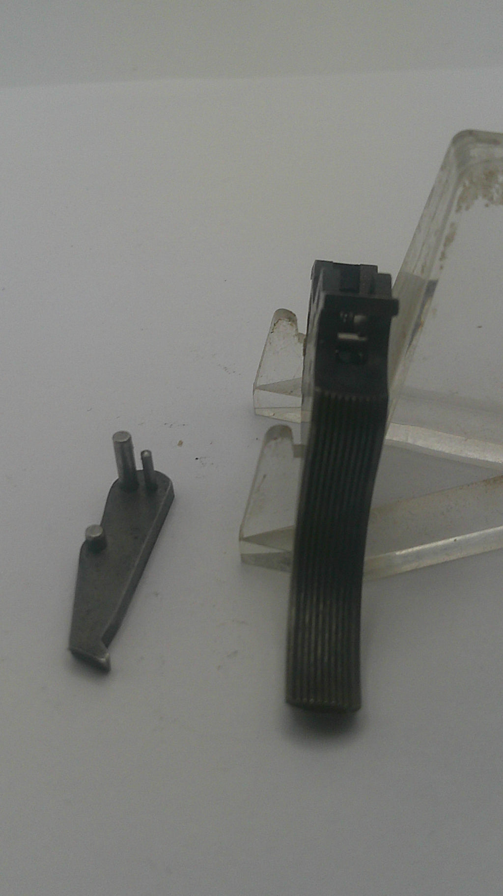 A small dark metal hardware component with a flat ribbed black strip across the middle, shown against a plain light gray background with a clear plastic stand.
