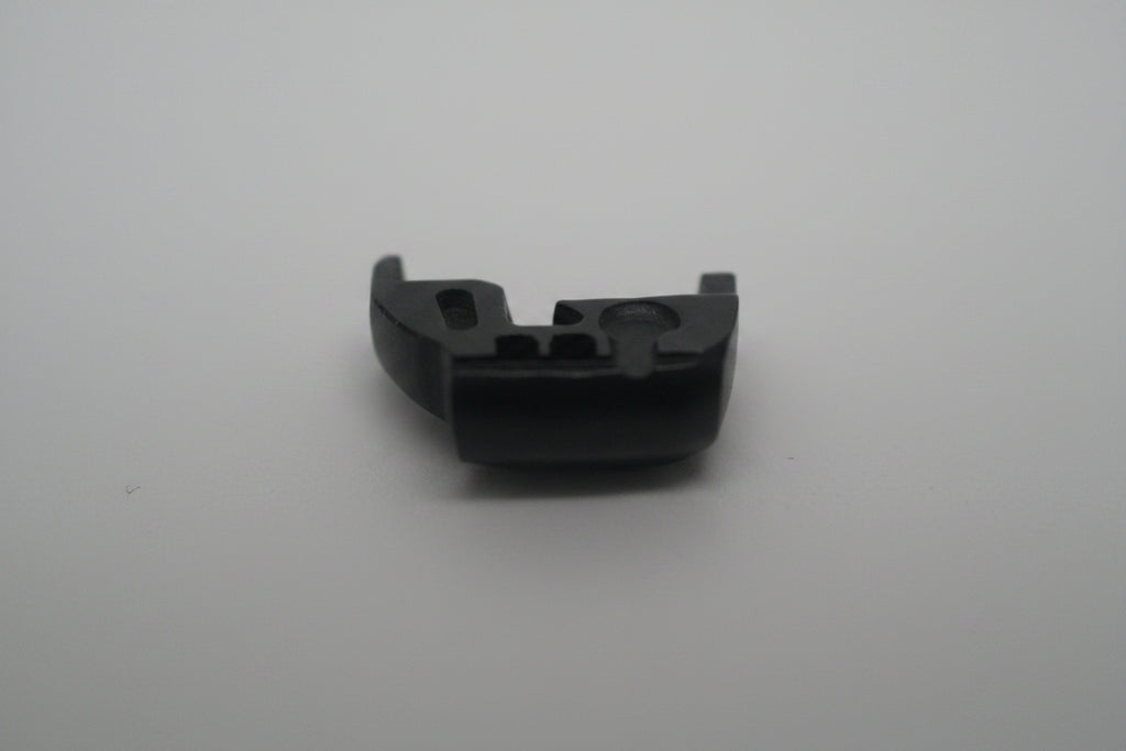 A small black plastic component or clip shown on a plain light background, with a faint pale object at the top edge.