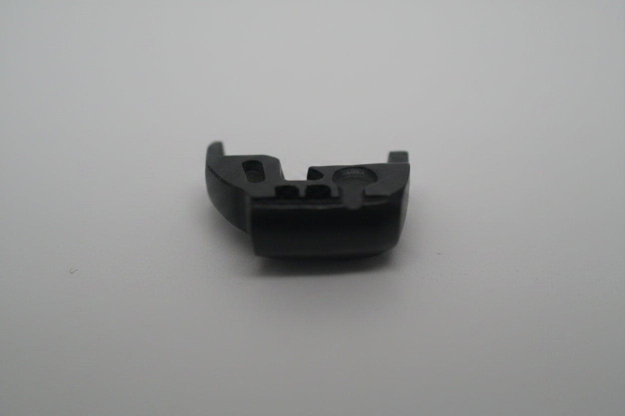 A small black plastic component or clip shown on a plain light background, with a faint pale object at the top edge.