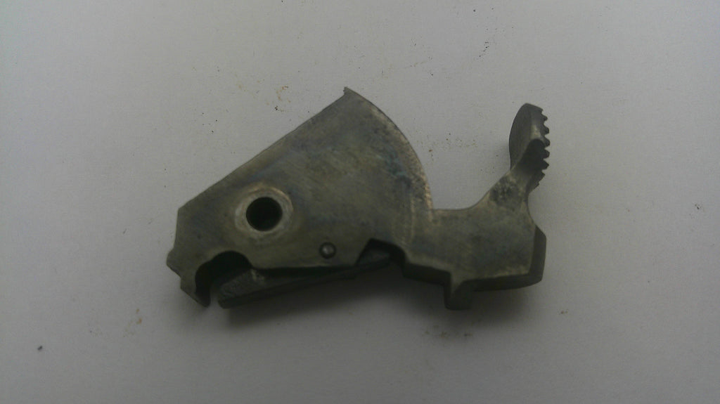 A small metallic mechanical part with a textured, weathered finish, photographed on a plain off-white surface.