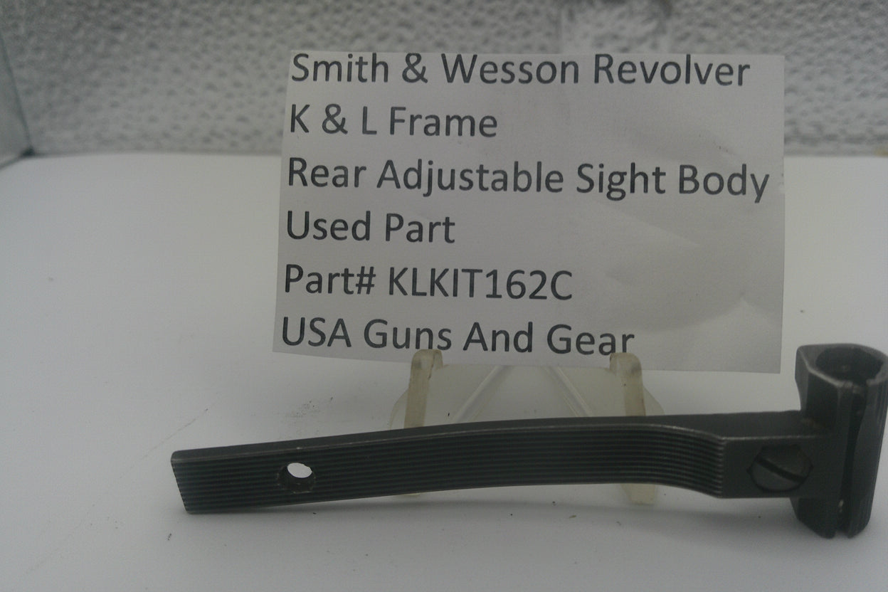 A used black metal part for a Smith & Wesson revolver rear adjustable sight body, displayed on a clear stand with a white label card showing part details.