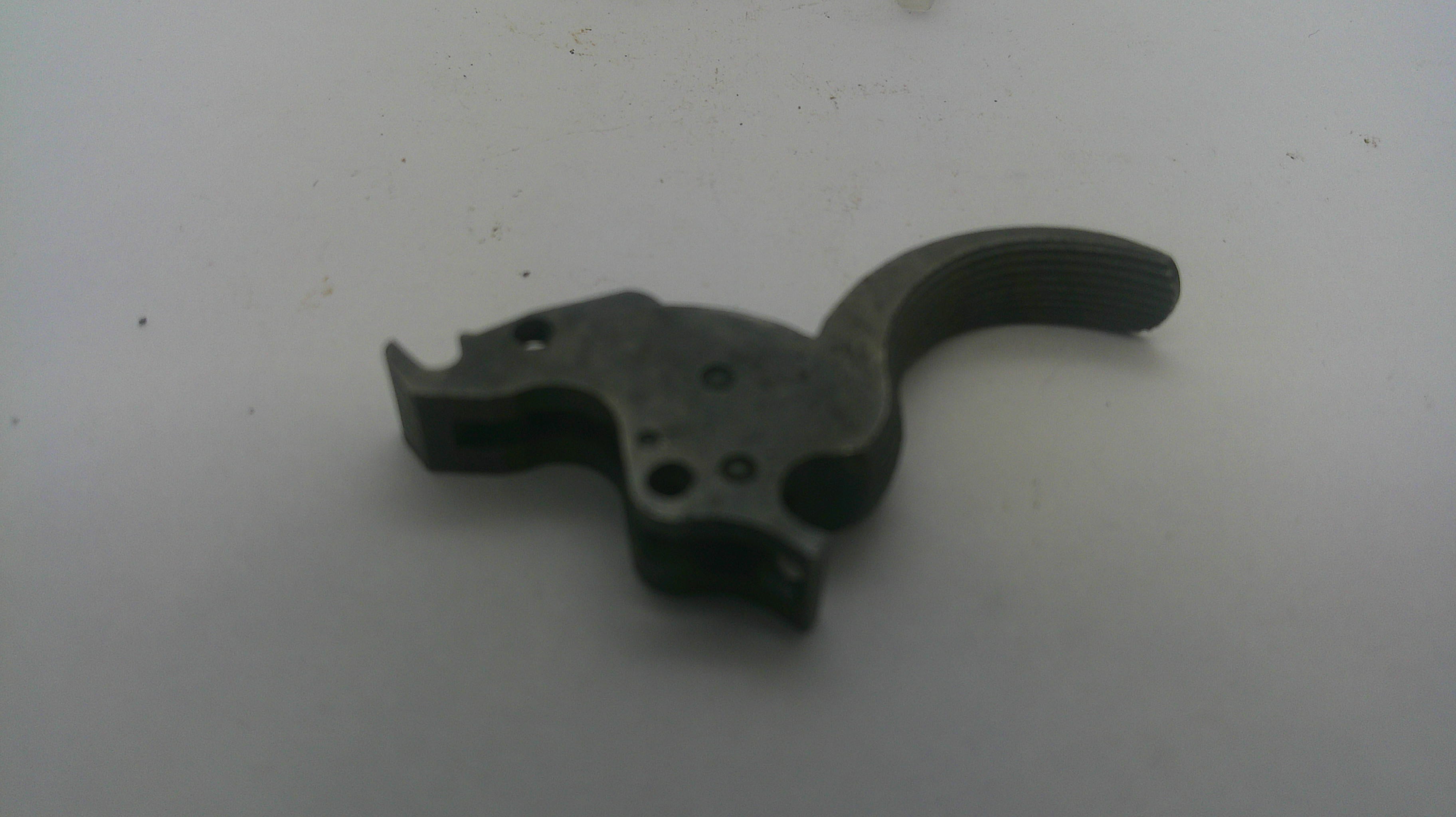 A dark metal firearm trigger assembly component, photographed on a plain light gray surface.