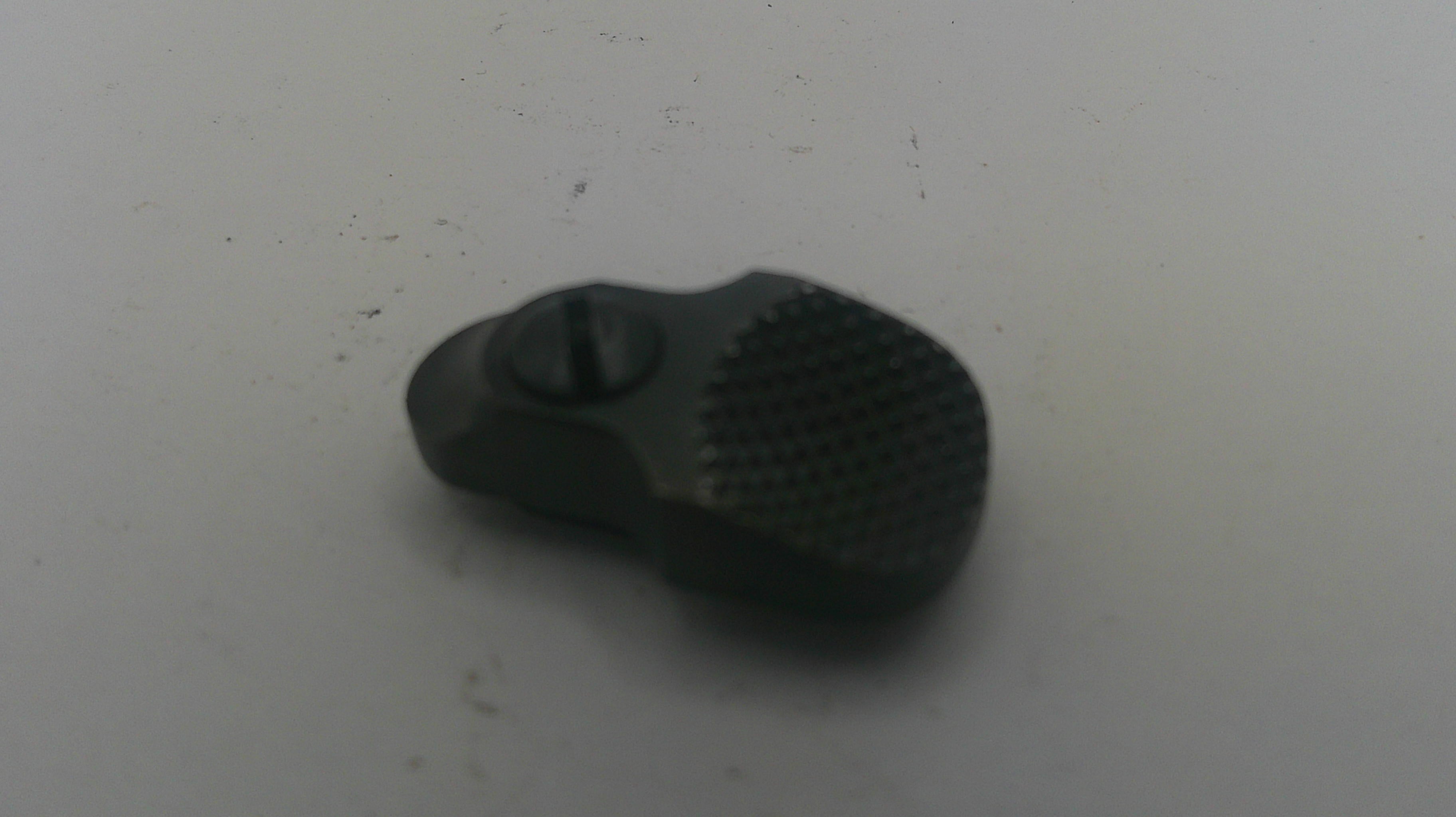 A small black textured plastic or rubber component with a central screw, photographed on a plain light gray surface.