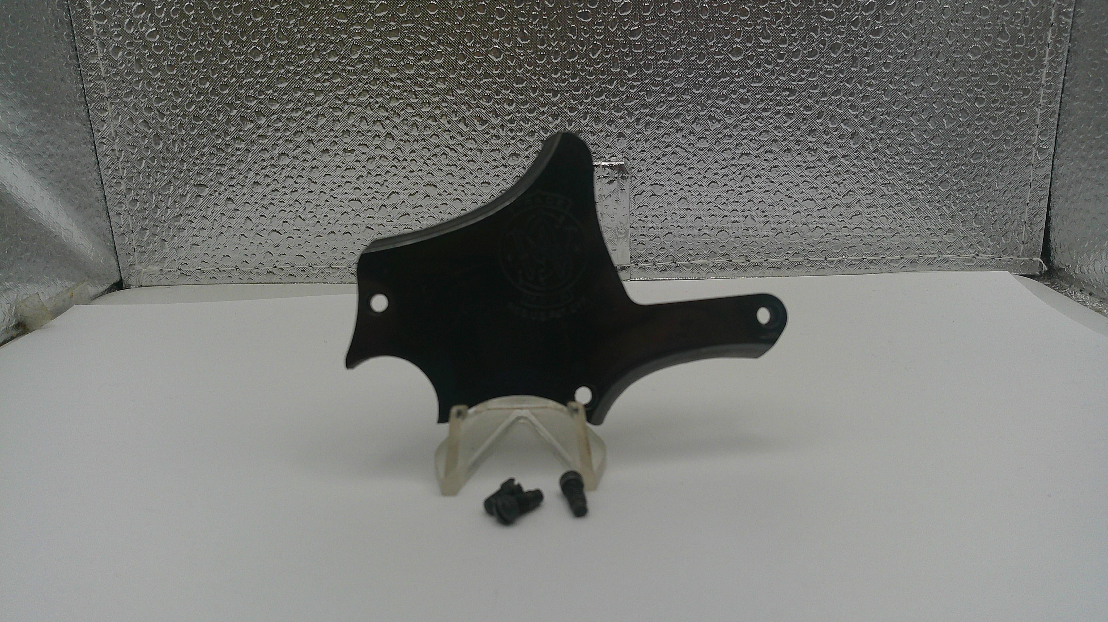 Black plastic component on a white stand with a textured gray background