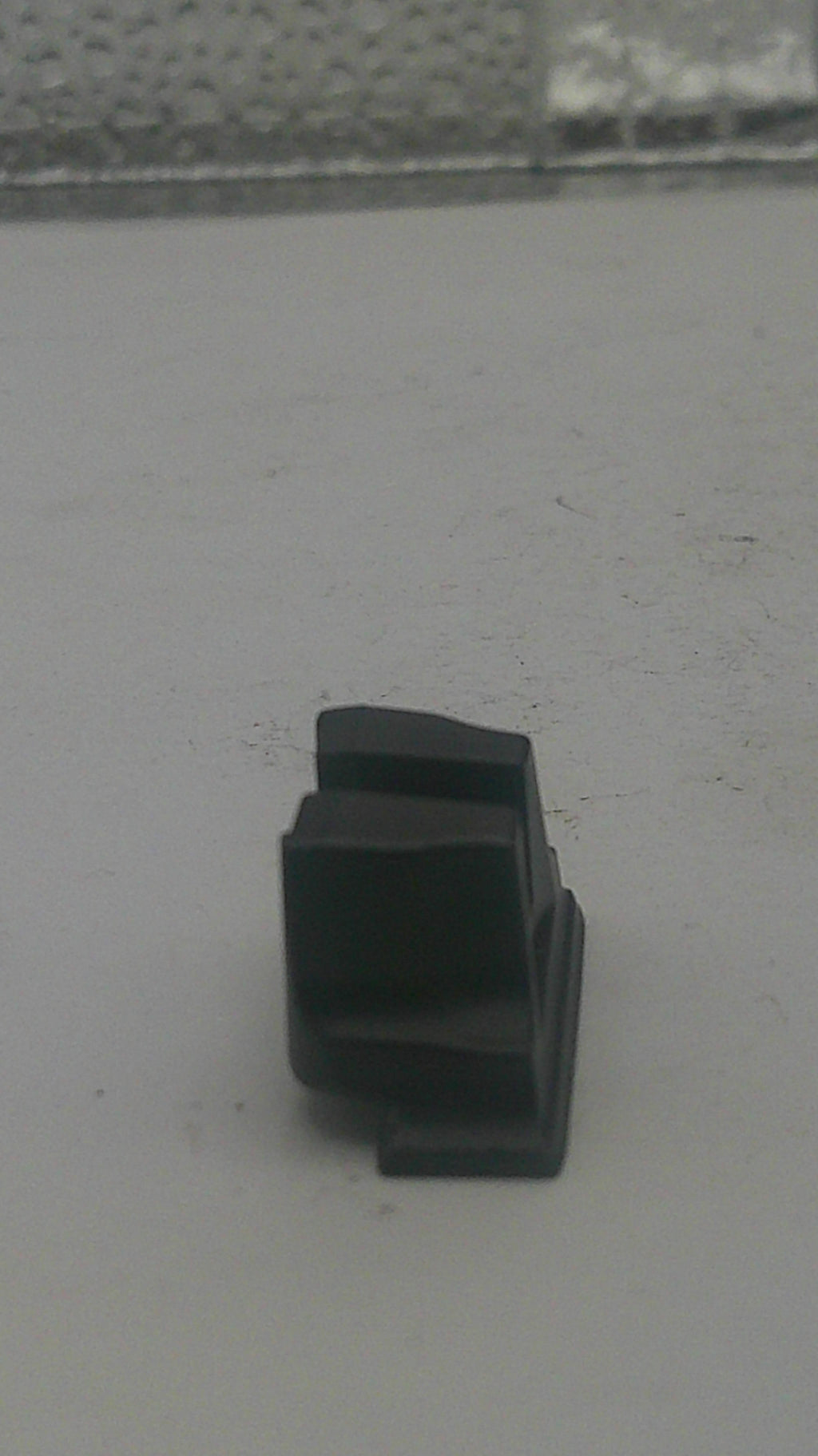 A small black plastic mounting bracket or clip attached to a light gray textured surface.