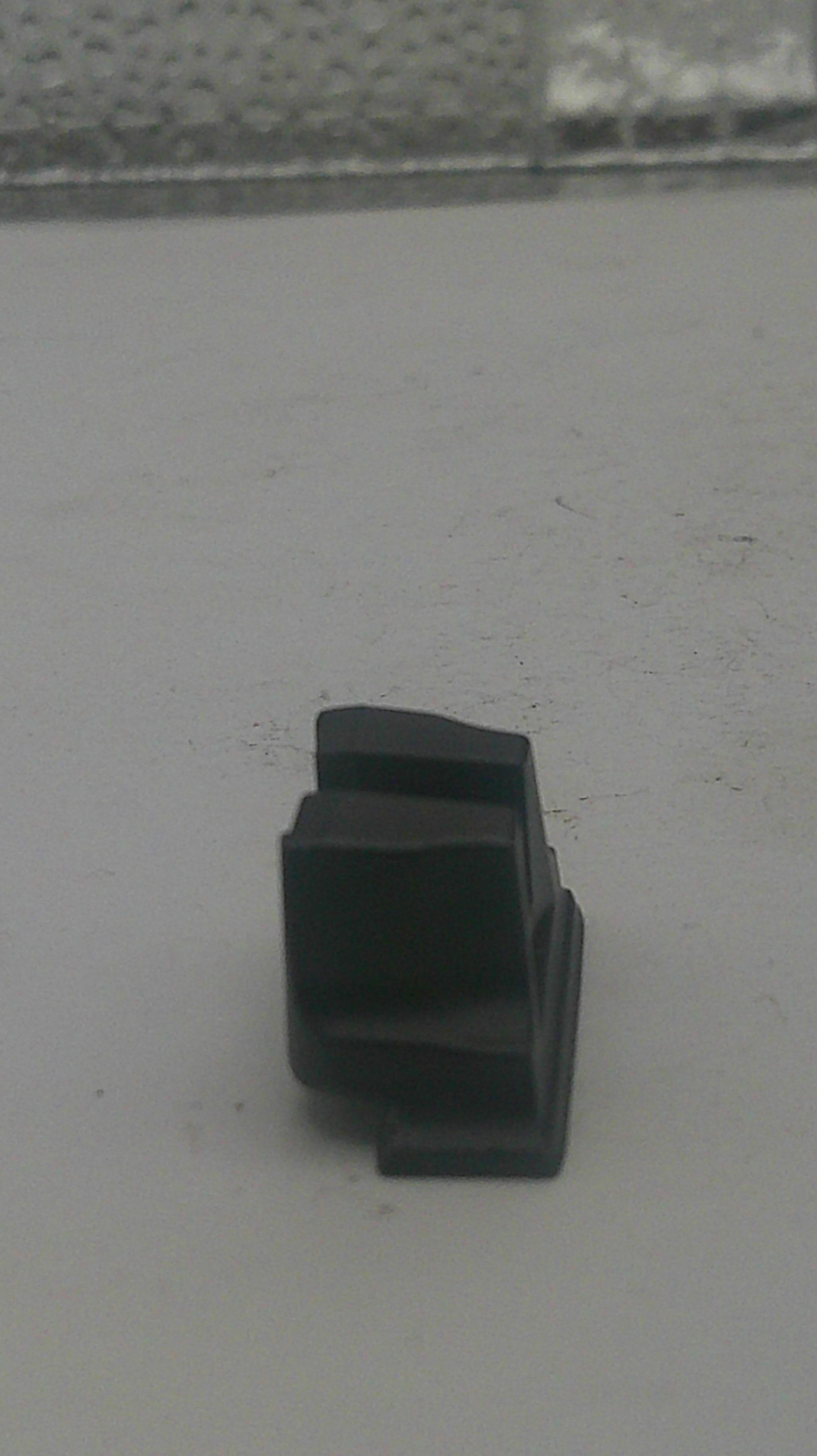 A small black plastic mounting bracket or clip attached to a light gray textured surface.