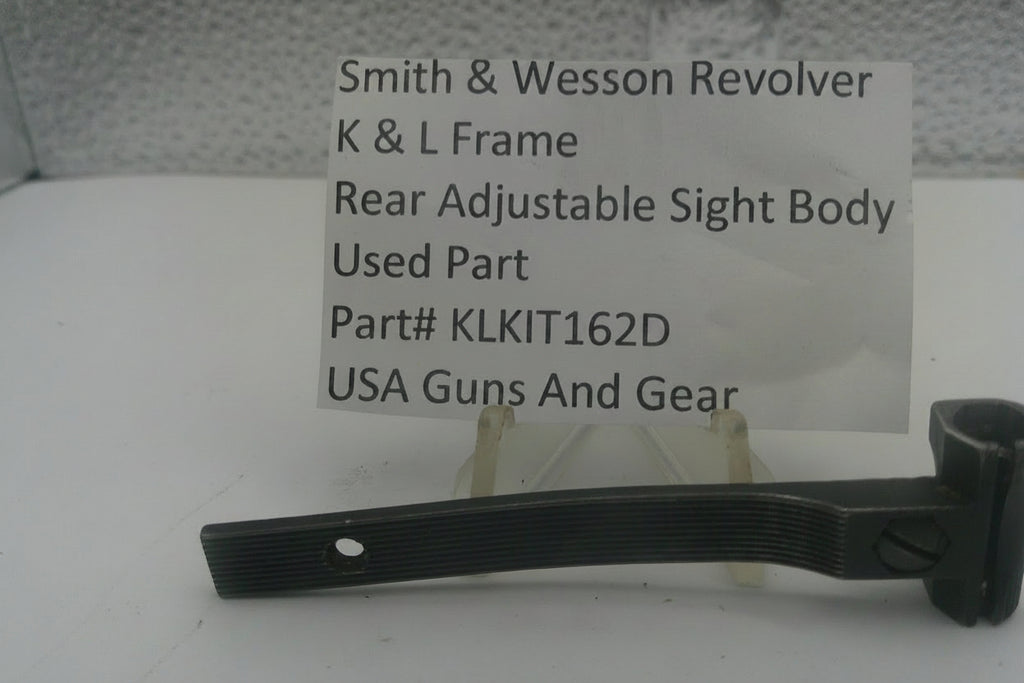 A used black metal part for a Smith & Wesson revolver rear adjustable sight body, displayed on a clear stand with a white label card showing part details.