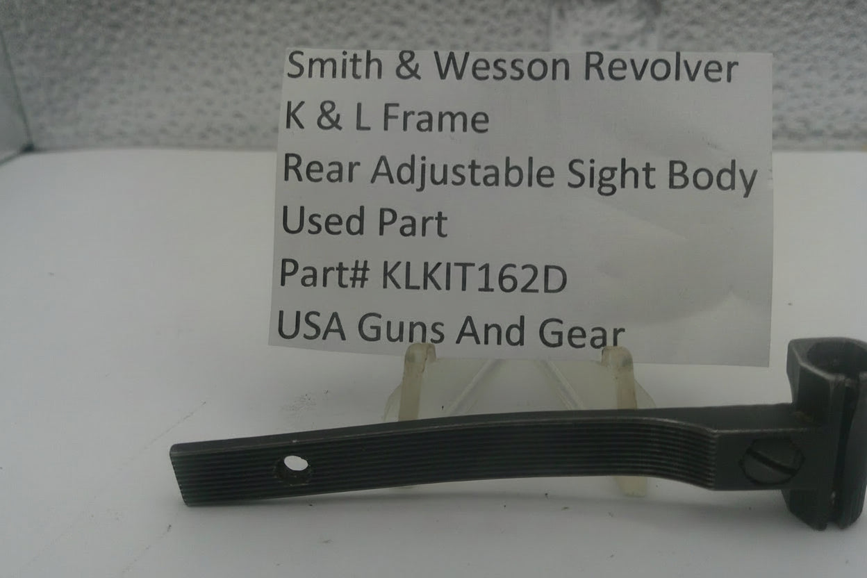 A used black metal part for a Smith & Wesson revolver rear adjustable sight body, displayed on a clear stand with a white label card showing part details.