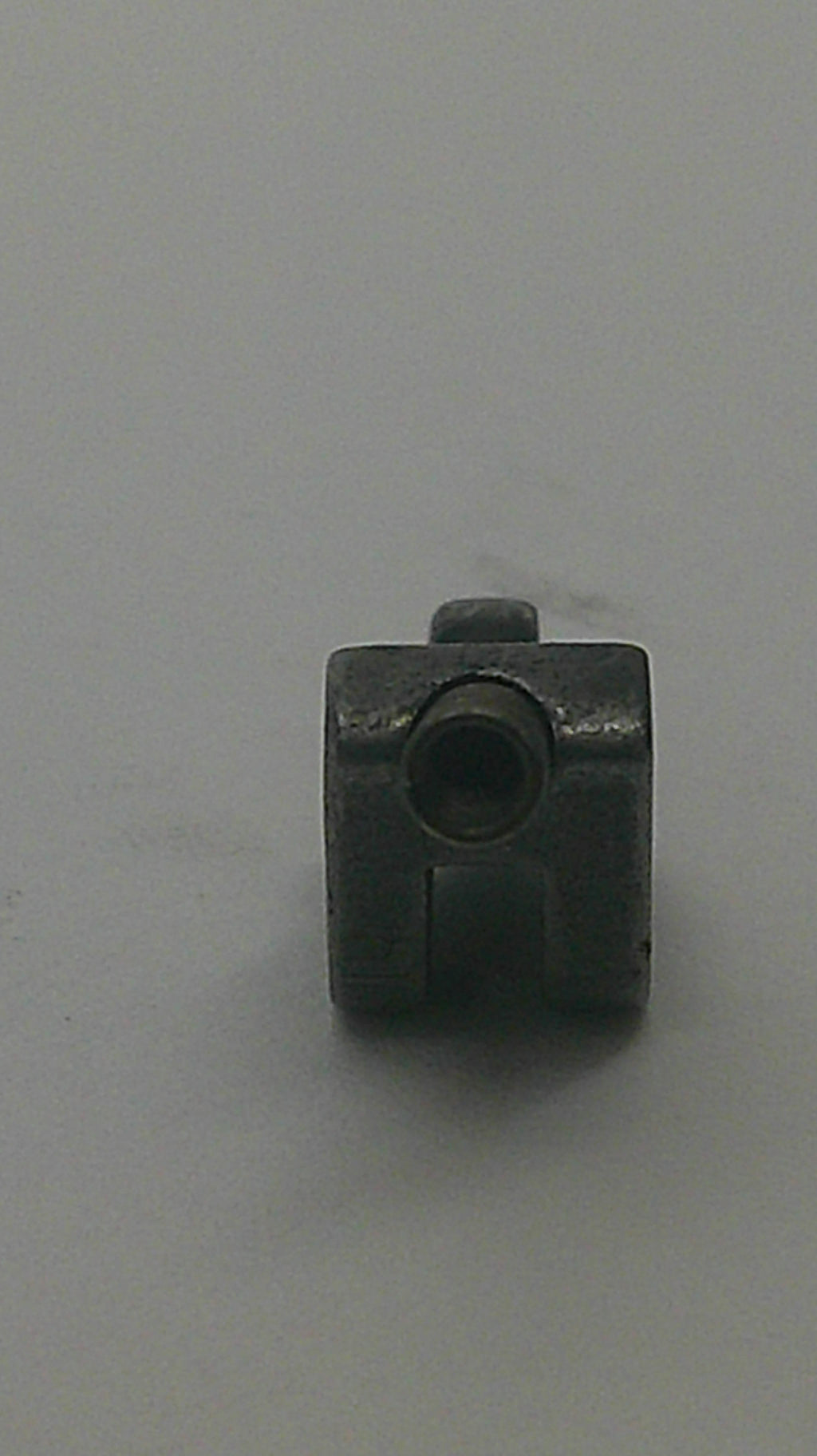 A small dark metal hardware component with a square shape, a circular hole, and a protruding tab, shown on a plain light gray background.