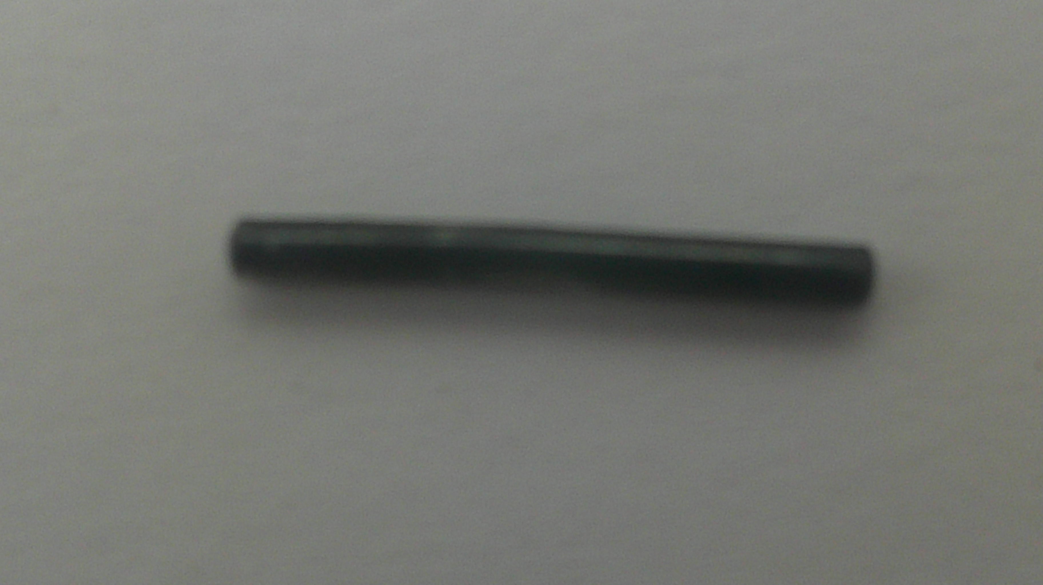 A small, dark metallic cylindrical rod or pin lying horizontally on a plain light gray background.