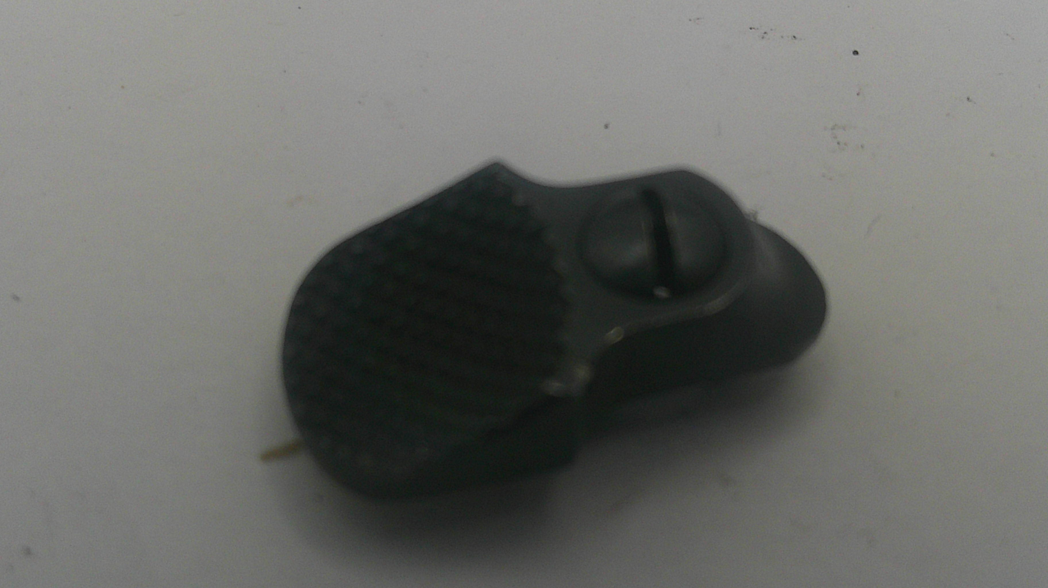 A small black textured plastic component with a screw, photographed on a plain light gray surface.