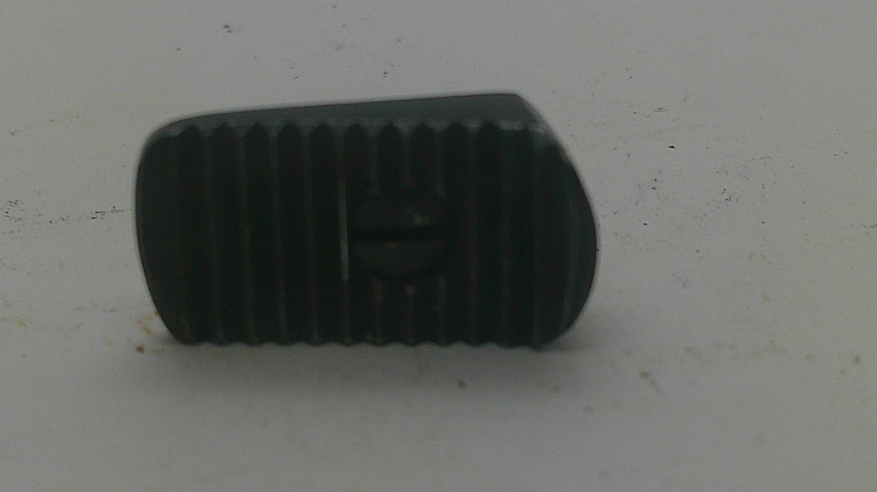 A small black textured plastic or rubber component with a central screw hole, photographed on a plain off-white surface.