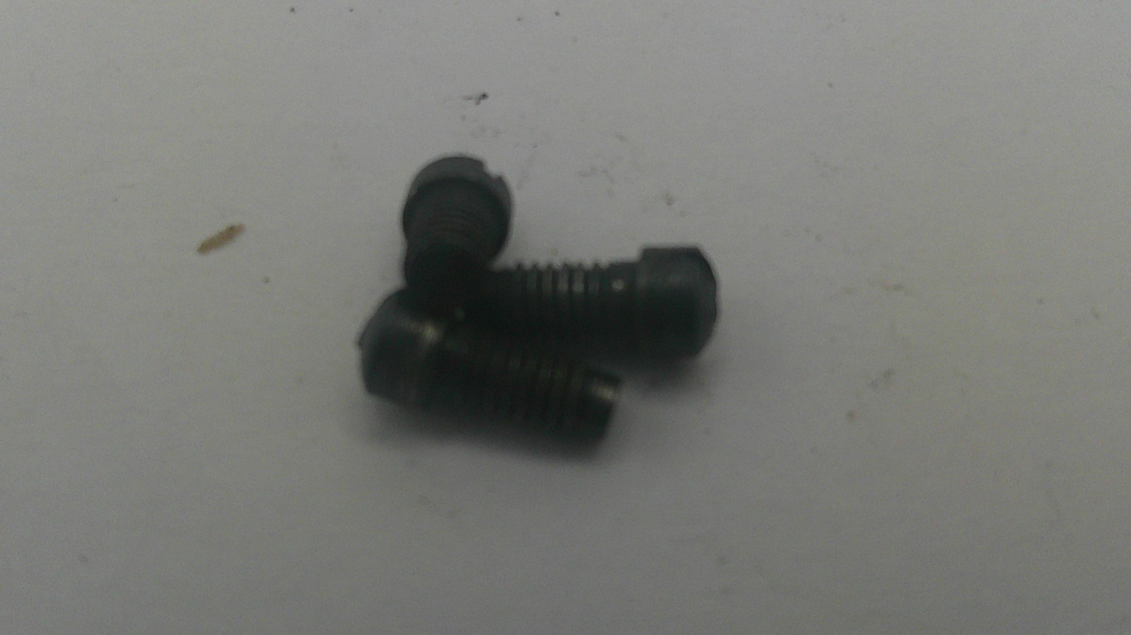 Three small black metal screws with slotted heads, arranged on a plain light gray surface.