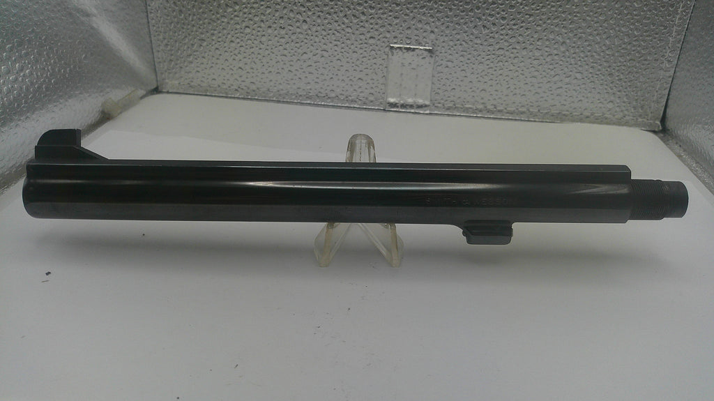 A black metal cylindrical component, likely a barrel or tube, displayed horizontally on a small clear stand against a textured silver backdrop.
