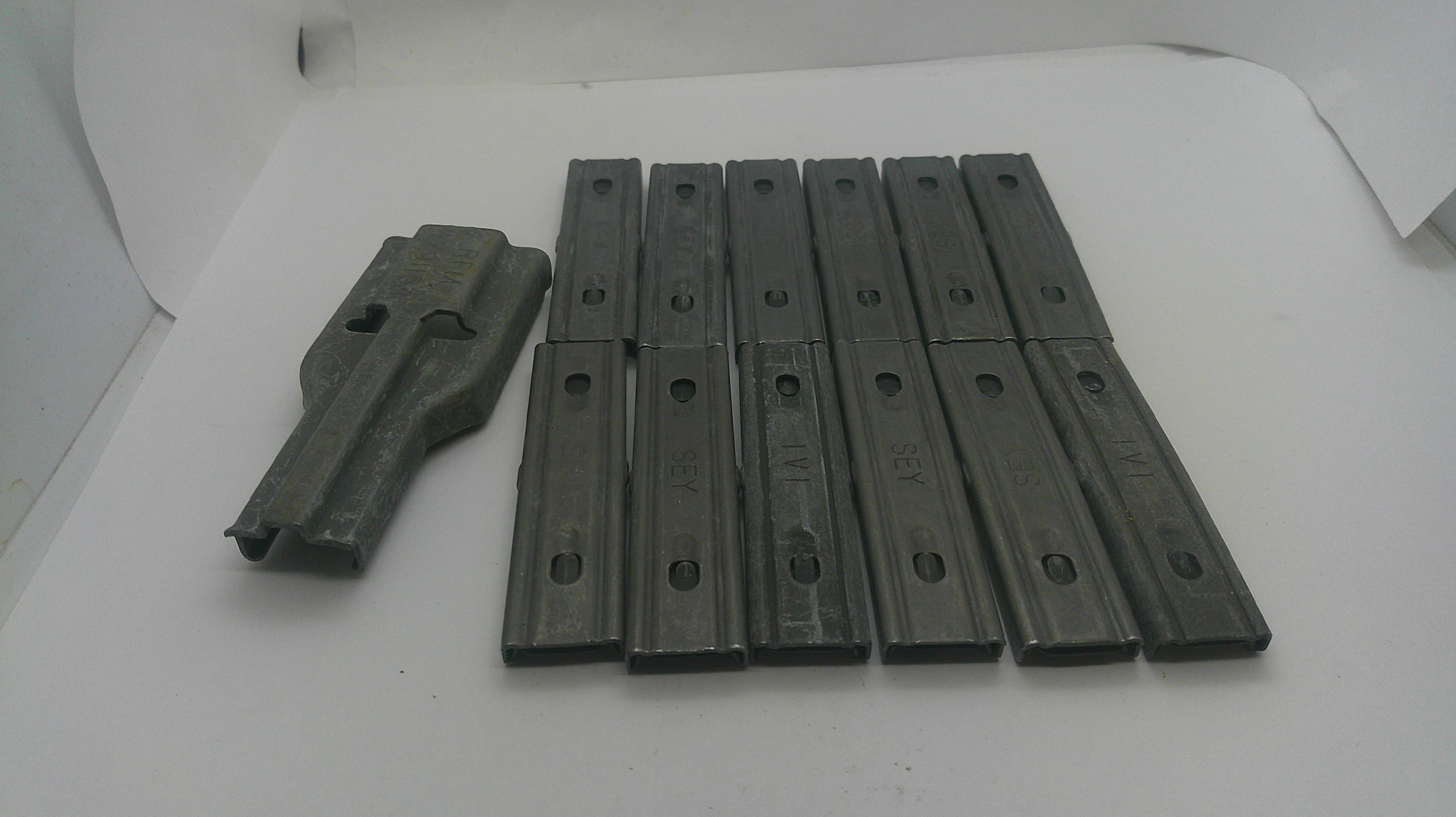 A set of dark gray metal guide rails or sliders, including one larger piece and nine matching narrow pieces, arranged on a white surface.