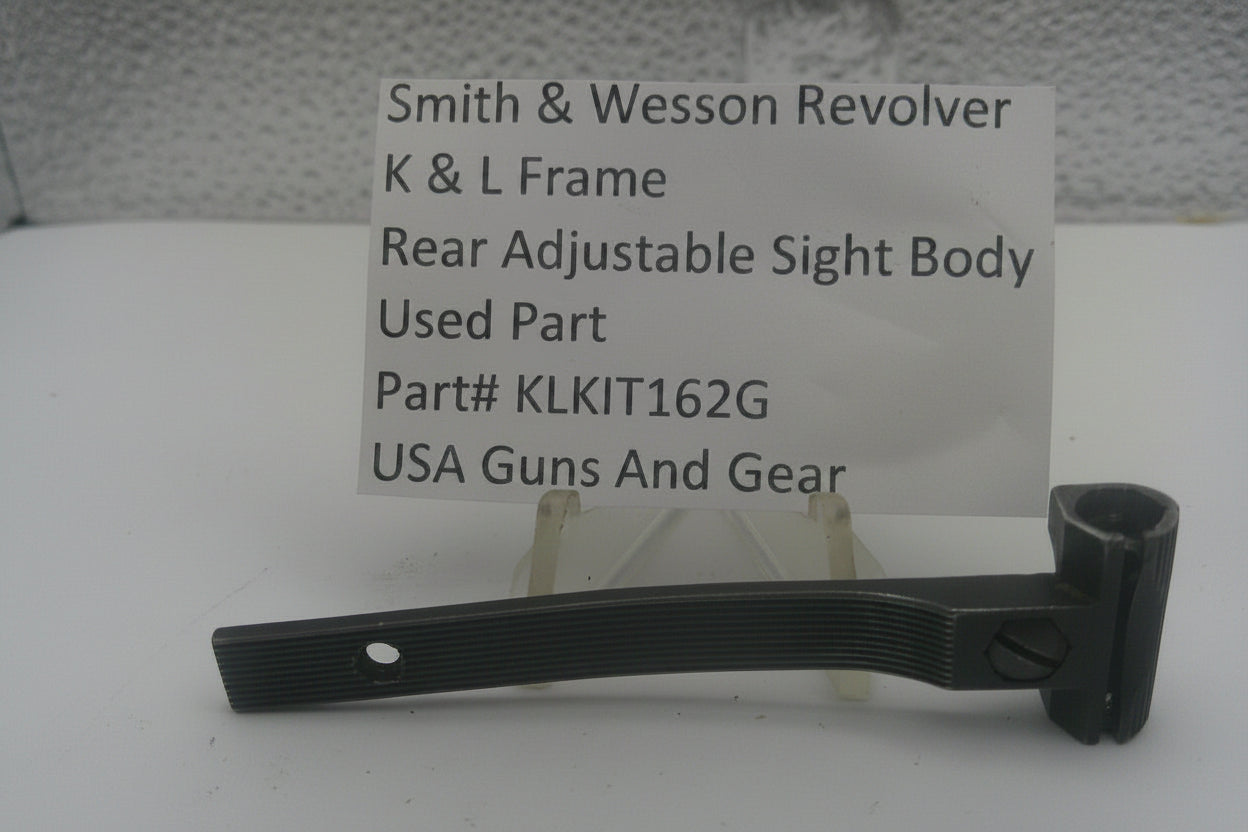 A used black metal part for a Smith & Wesson revolver rear adjustable sight body, displayed on a clear stand with a white label card showing part details.