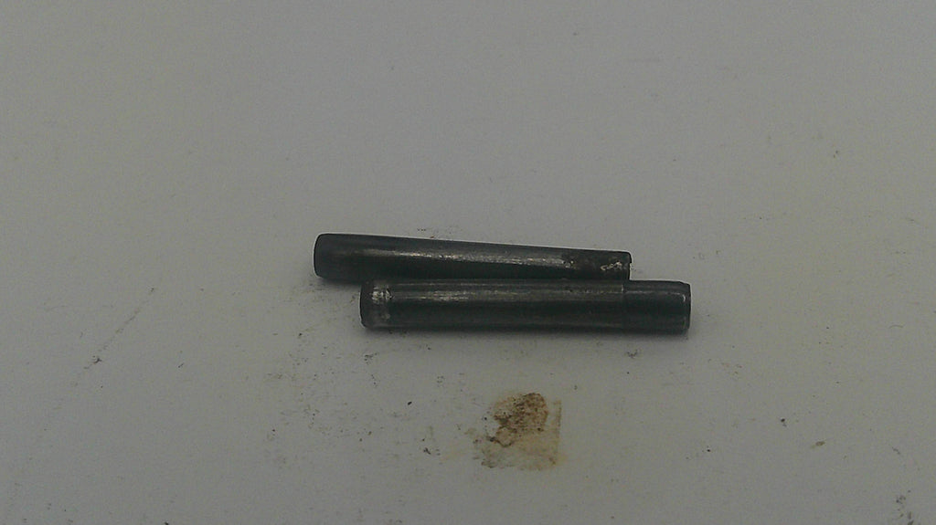 Two small dark metal cylindrical pins or rods placed on a plain off-white surface.
