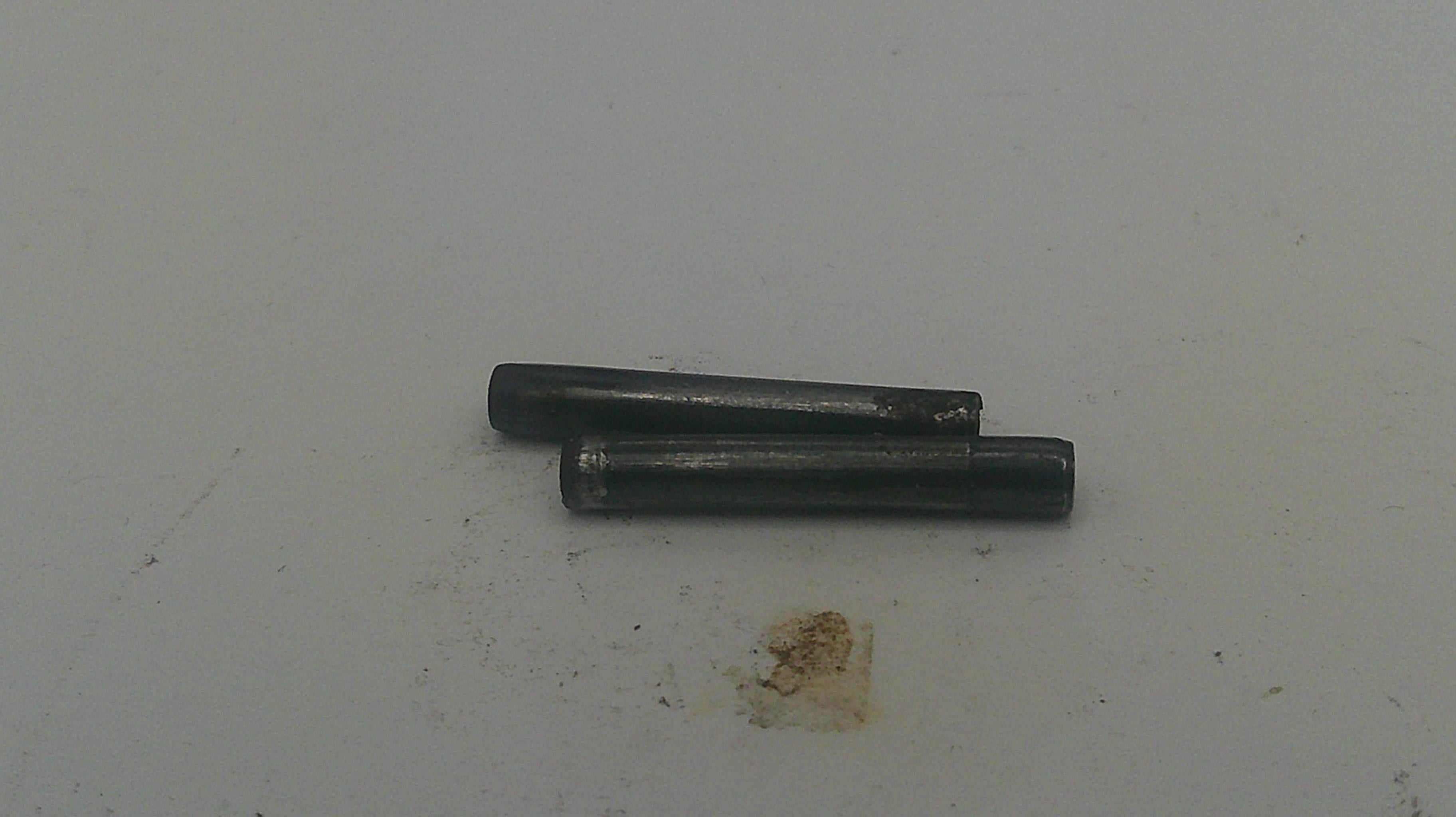 Two small dark metal cylindrical pins or rods placed on a plain off-white surface.