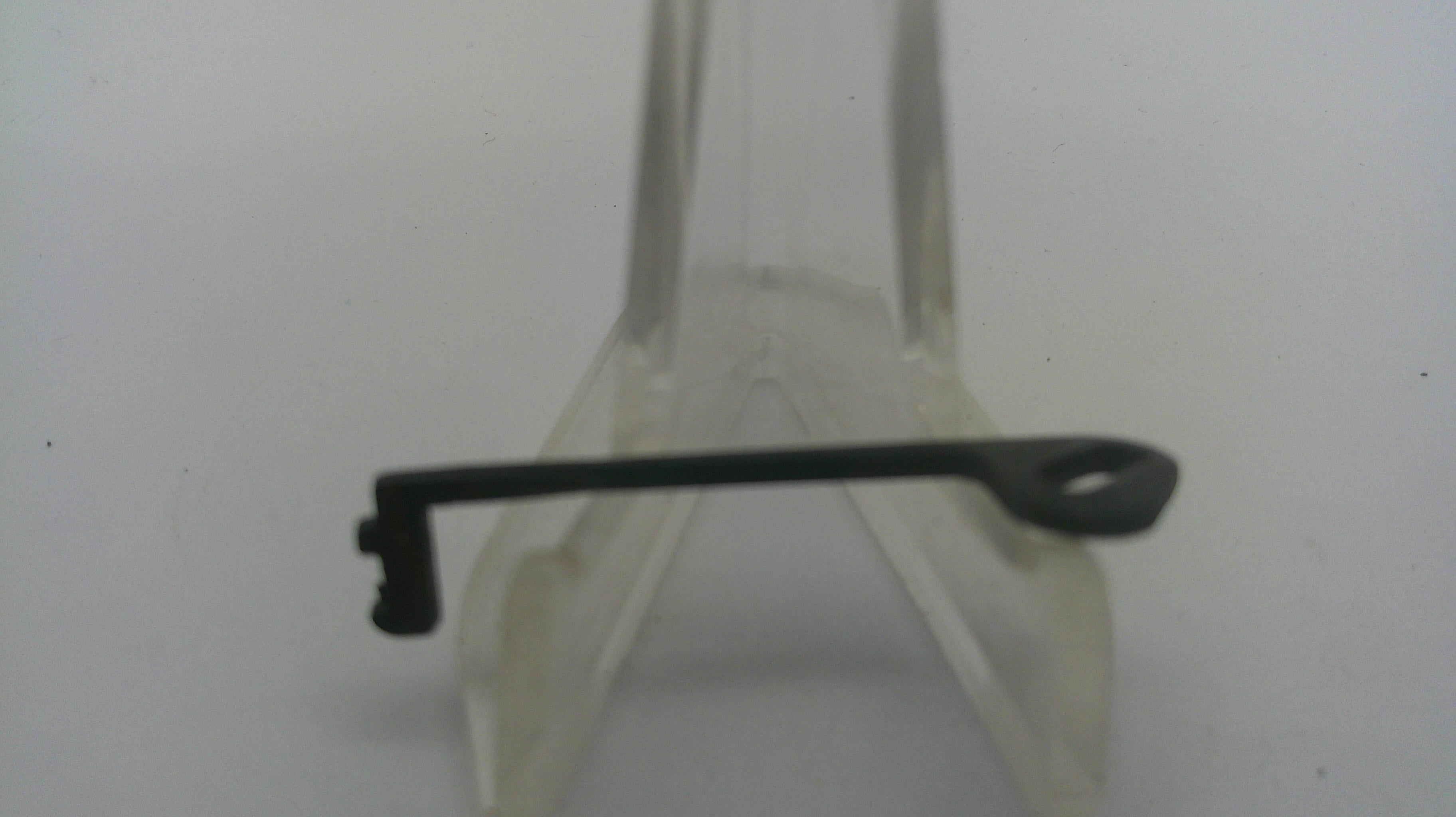 A small black metal key or lock pick with a looped end, displayed on a clear plastic stand against a plain light background.