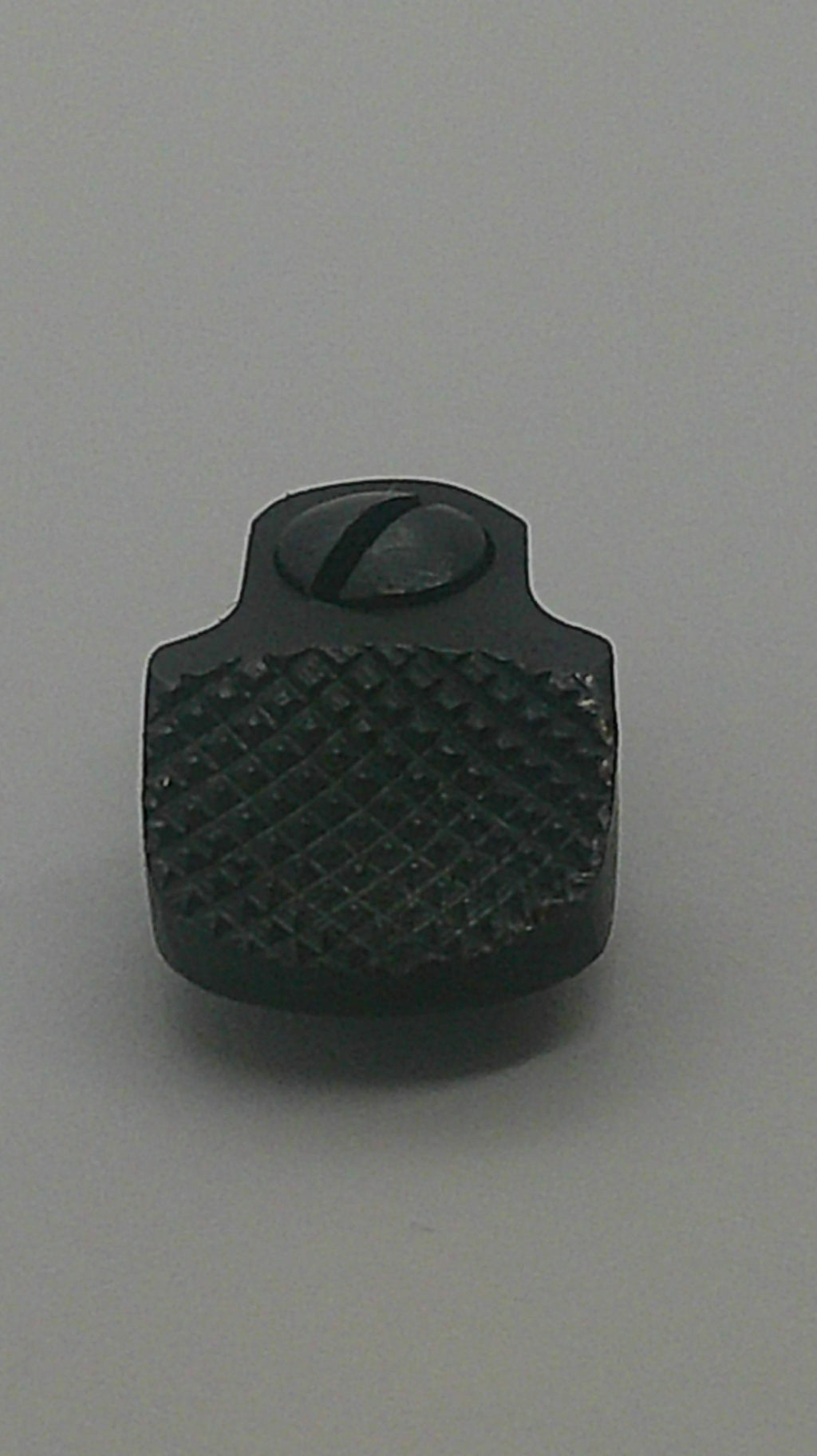 A small black textured plastic knob or dial with a knurled diamond pattern and a circular cutout, shown on a plain gray background.