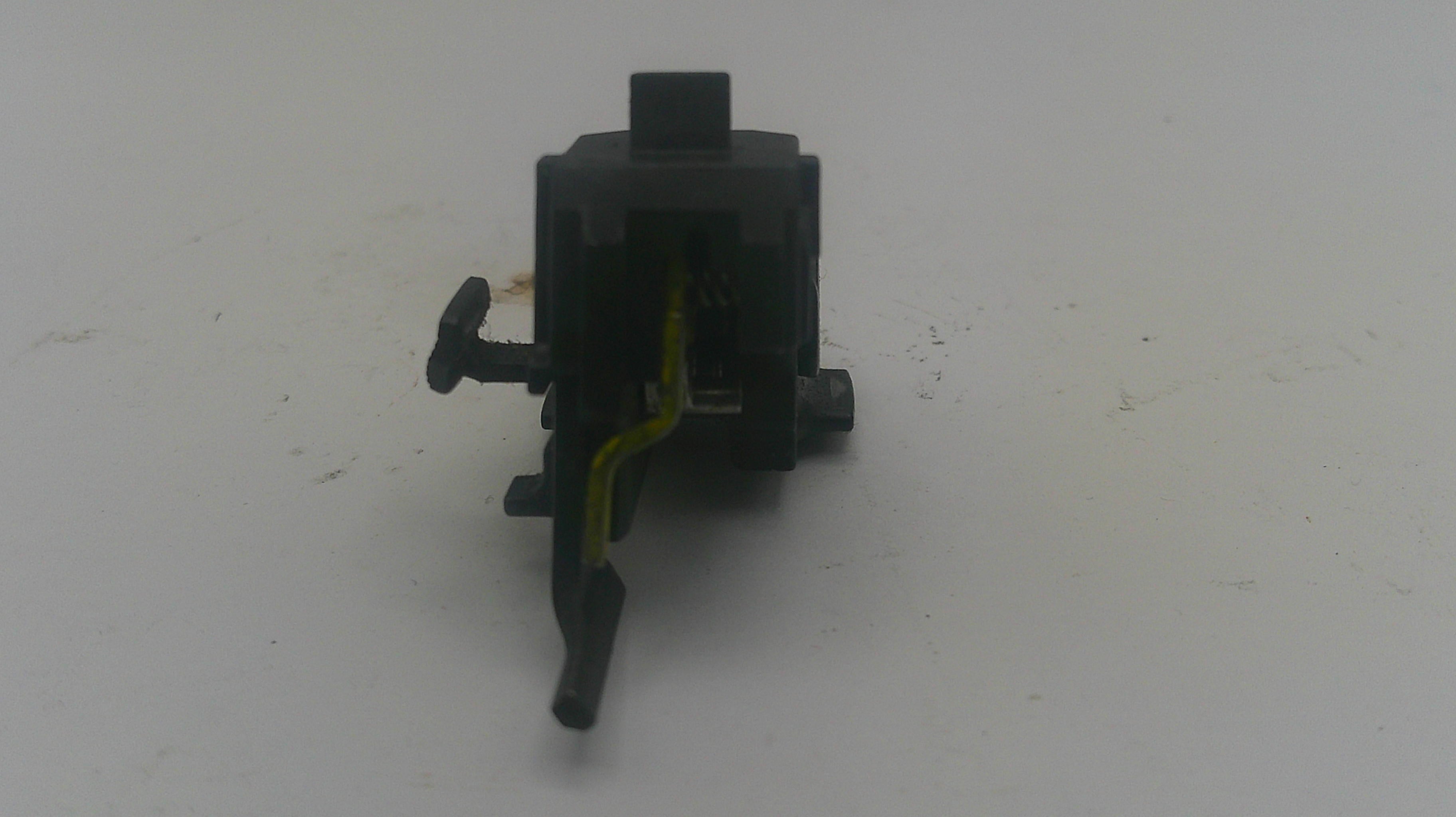 A small black plastic automotive or appliance switch component with a yellow wire attached, photographed on a plain light gray surface.