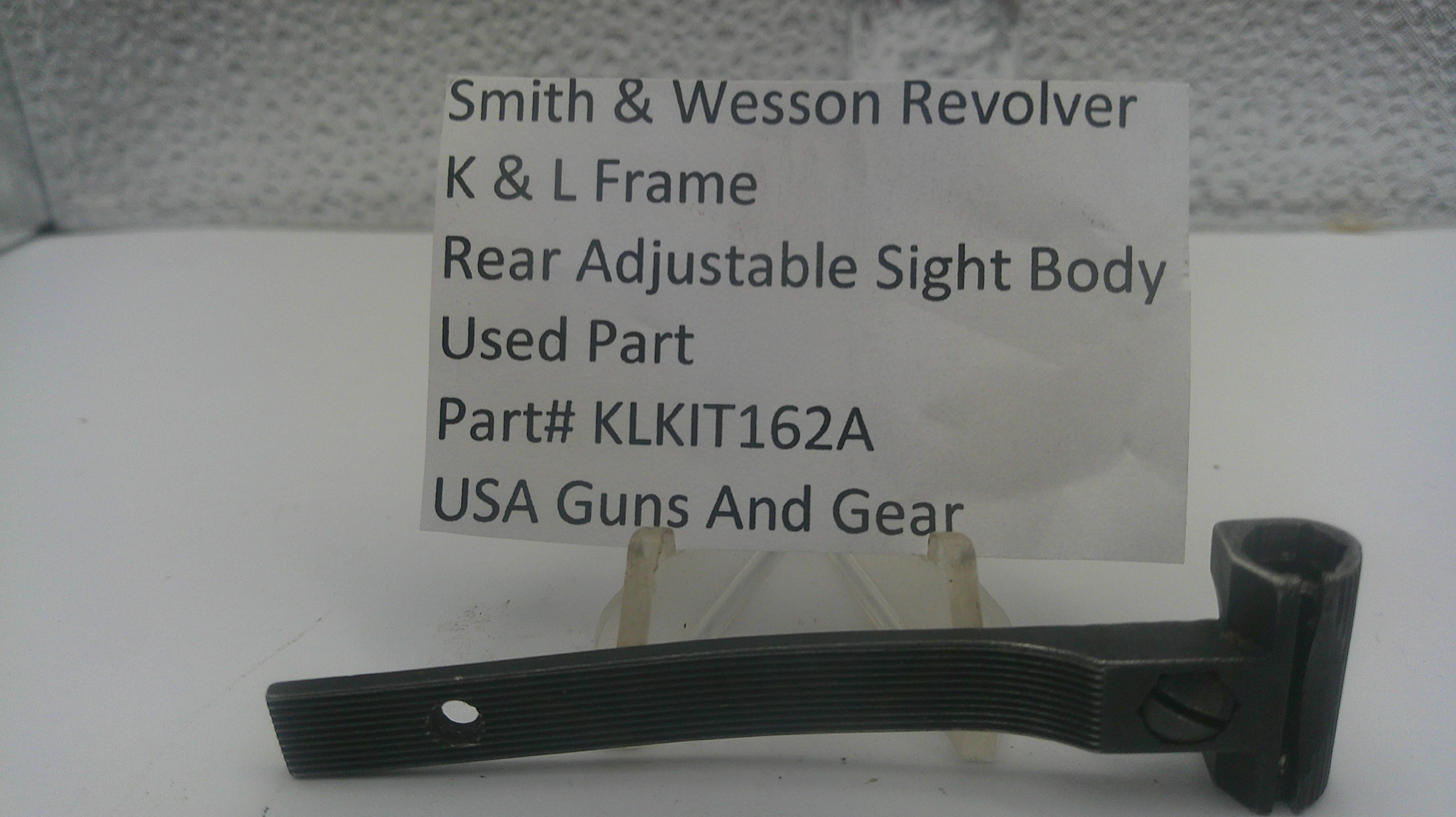 A used black metal part for a Smith & Wesson revolver rear adjustable sight body, displayed on a clear stand with a white label card showing part details.