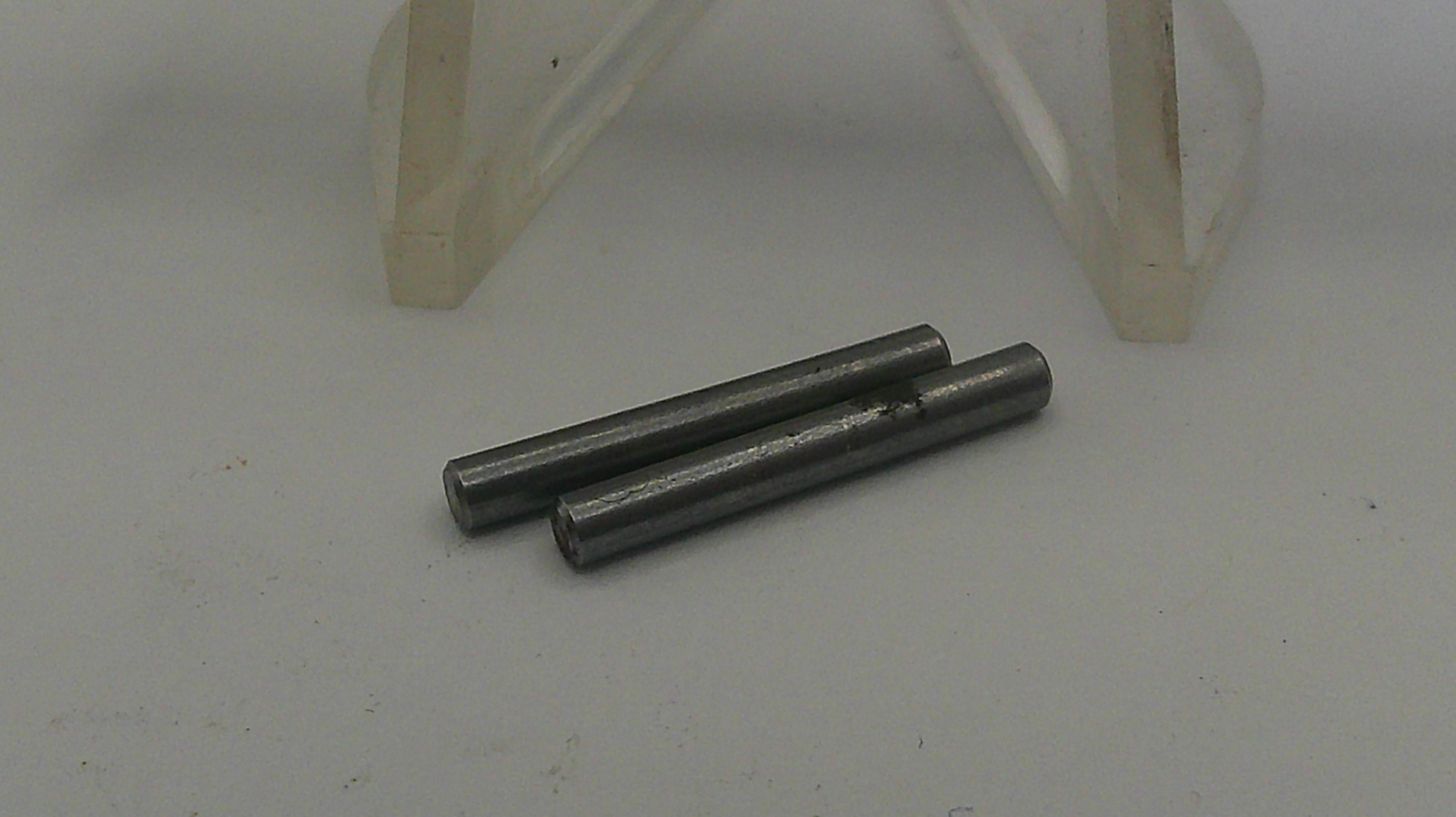 Three metal cylindrical objects on a white surface with a clear plastic object in the background.