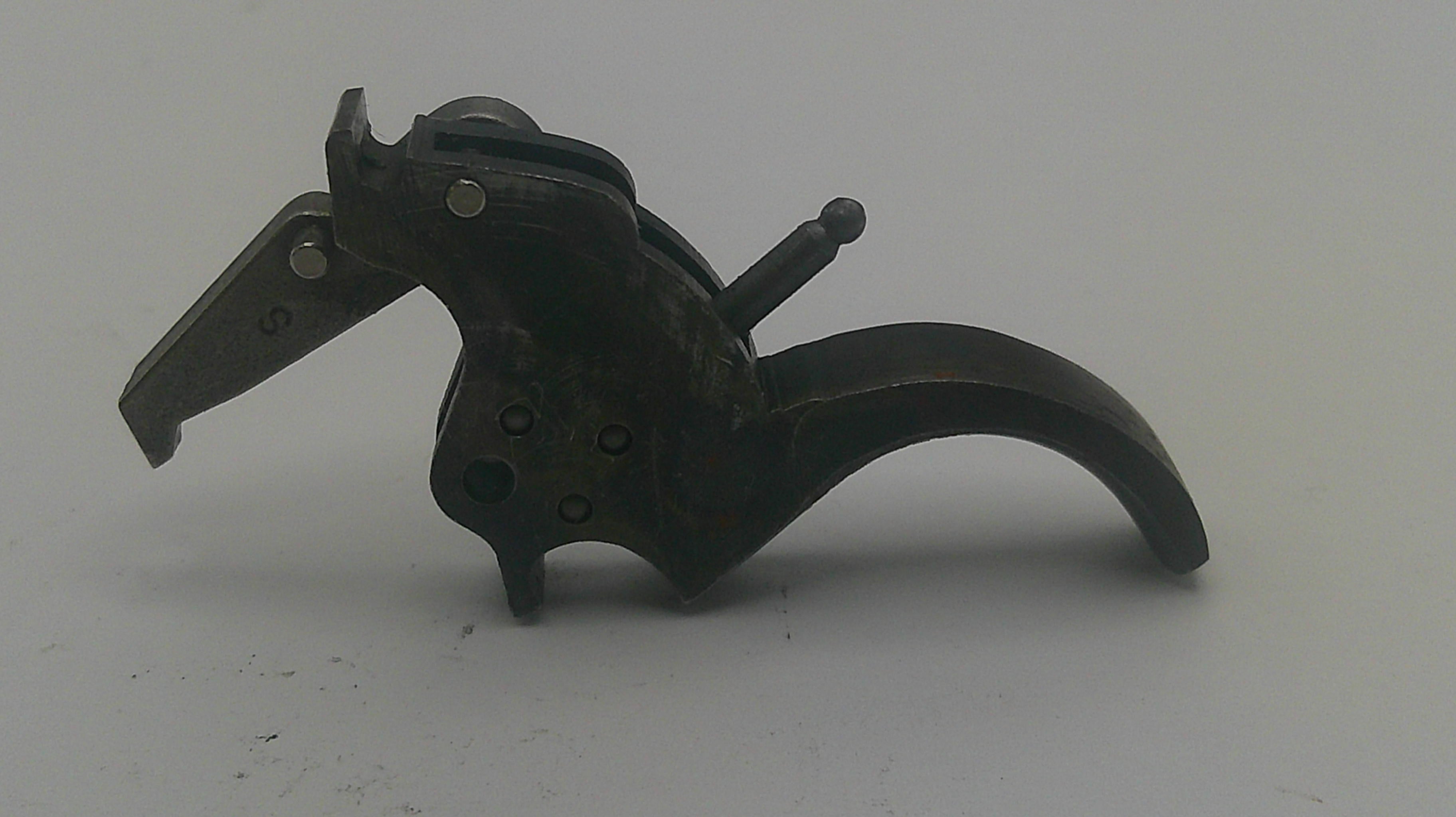 A dark metal mechanical trigger component with a curved lever and pivot screw, photographed on a plain light gray background.
