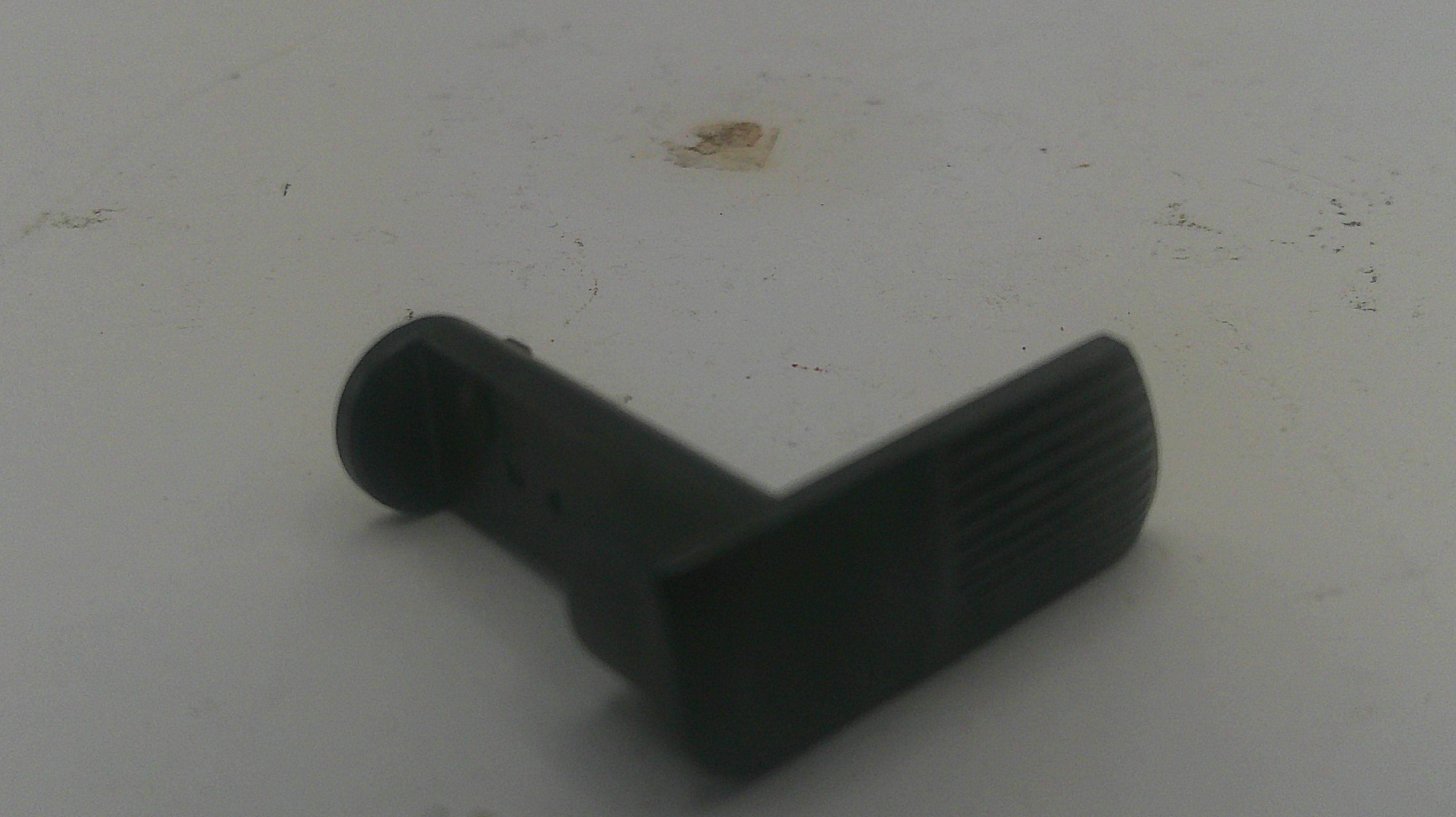 A small black plastic L-shaped component with a textured side, photographed on a light gray surface.