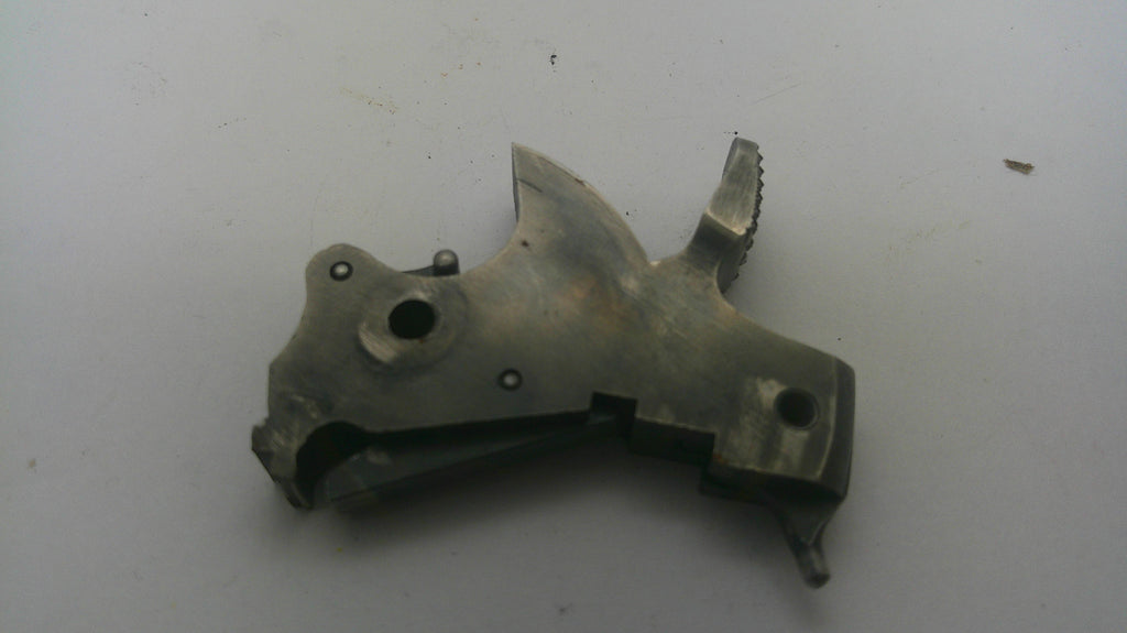 A used metal firearm trigger assembly, showing a weathered metallic finish with dark patina and wear, photographed on a plain off-white background.