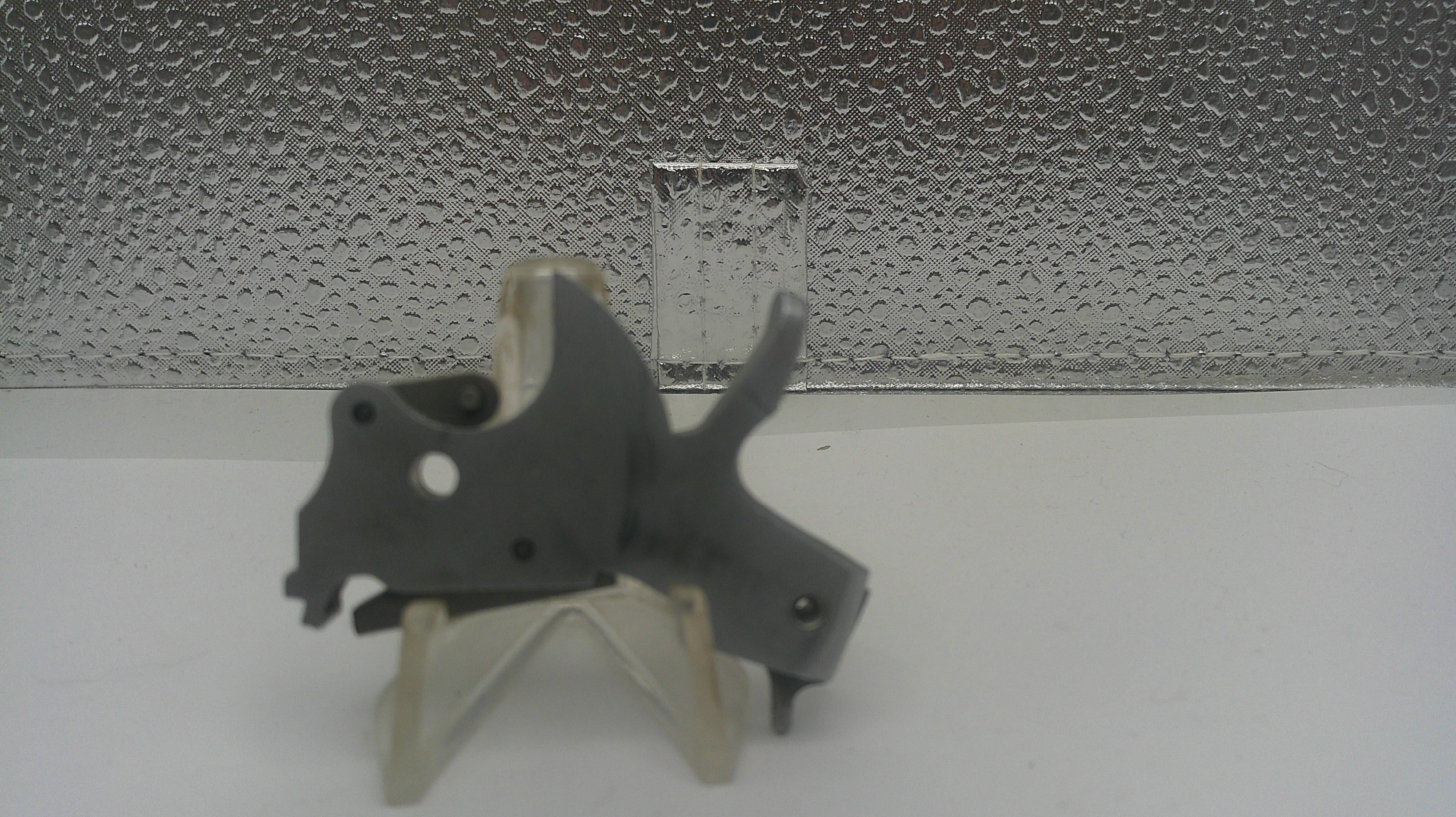Small gray mechanical object on a stand against a textured silver background