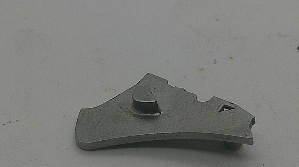 A small gray metal mechanical part or tool component with a curved shape, photographed on a plain light gray surface.