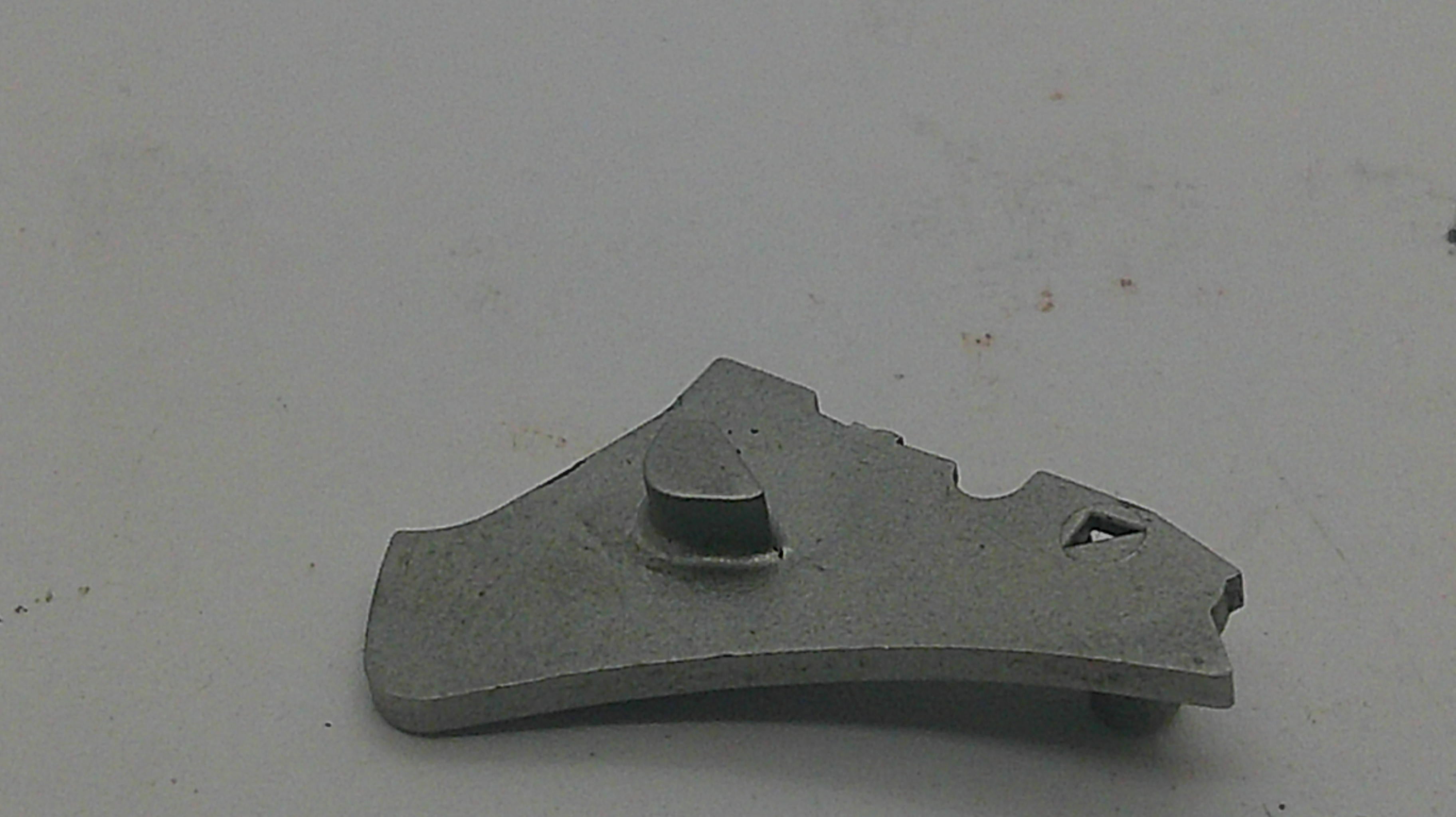 A small gray metal mechanical part or tool component with a curved shape, photographed on a plain light gray surface.