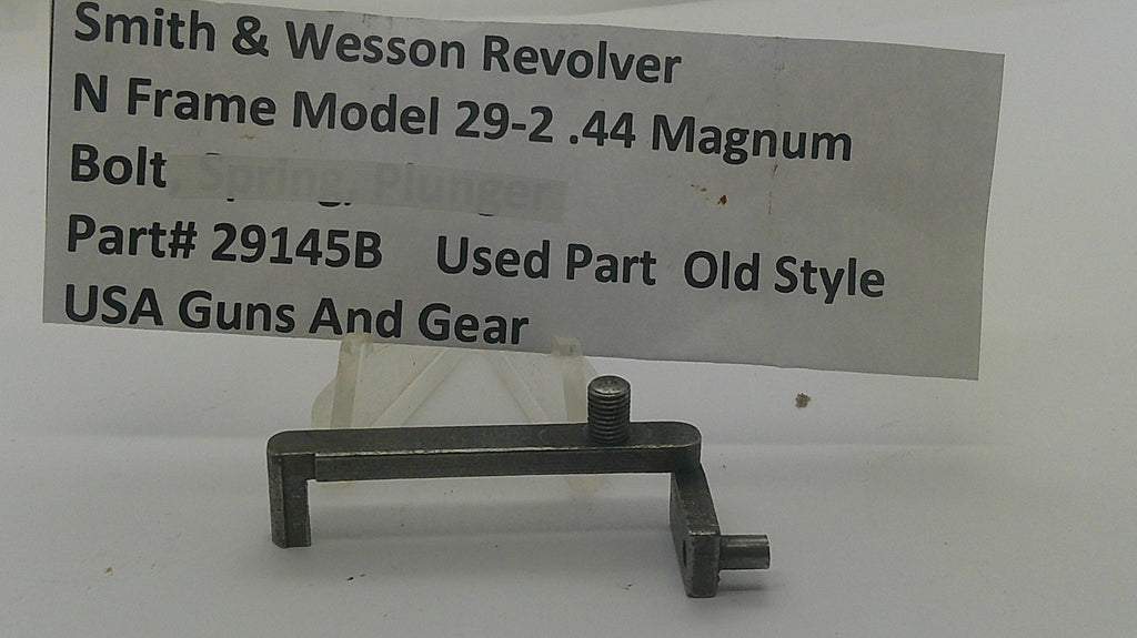 A used metal gun part, specifically a Smith & Wesson Revolver bolt spring plunger, displayed on a white surface with a paper label in the background containing part number 29145B.