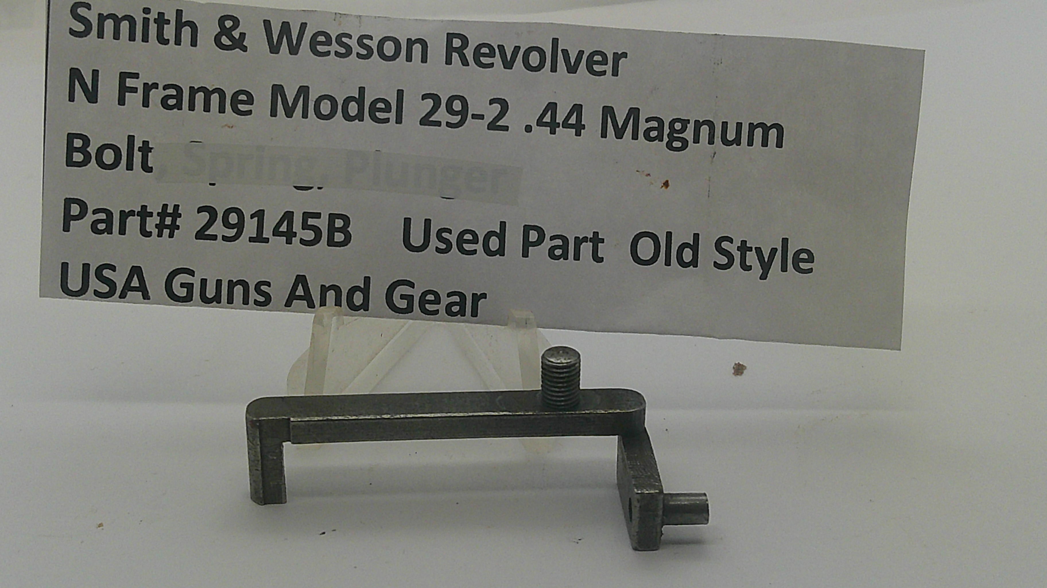 A used metal gun part, specifically a Smith & Wesson Revolver bolt spring plunger, displayed on a white surface with a paper label in the background containing part number 29145B.