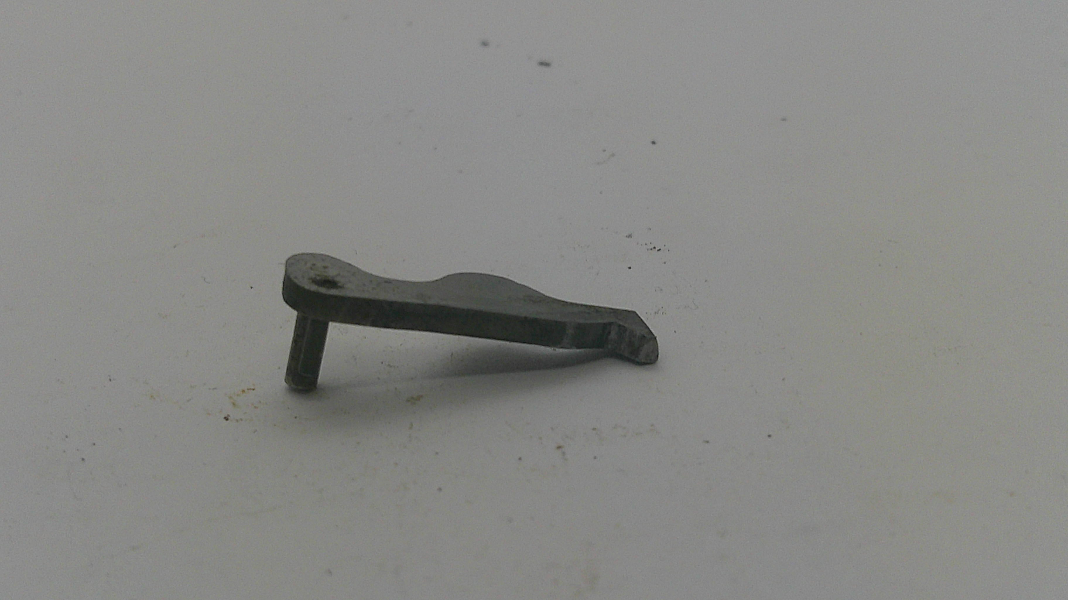 A small dark metal hardware piece, possibly a bracket or latch component, shown on a plain light gray surface.