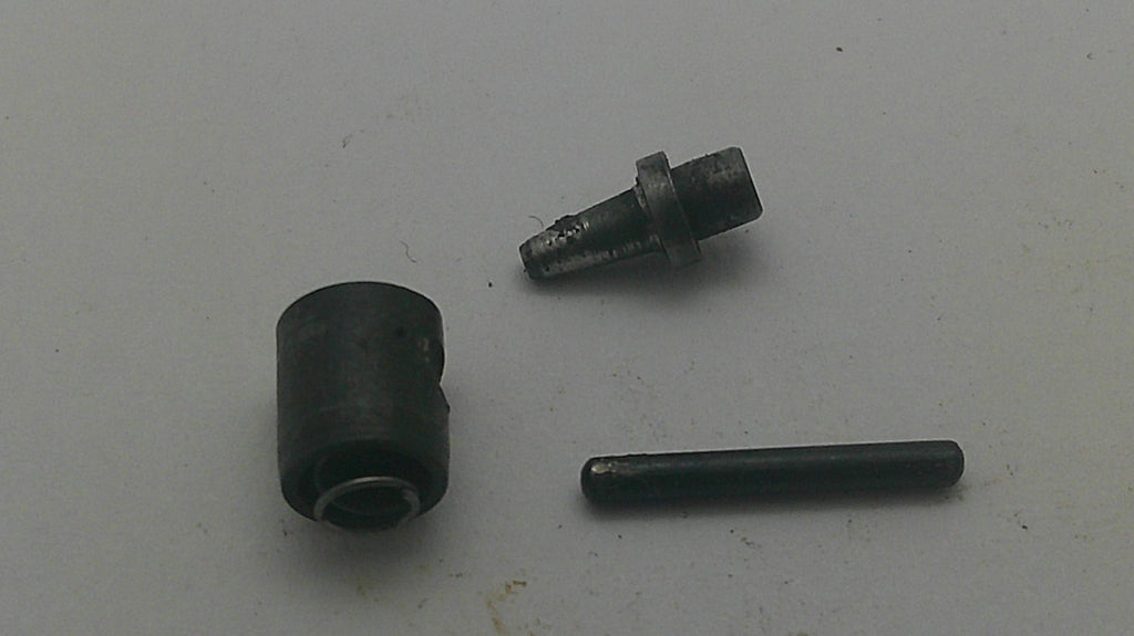 A small black cylindrical component and a separate dark metal pin or rod placed on a plain light background.