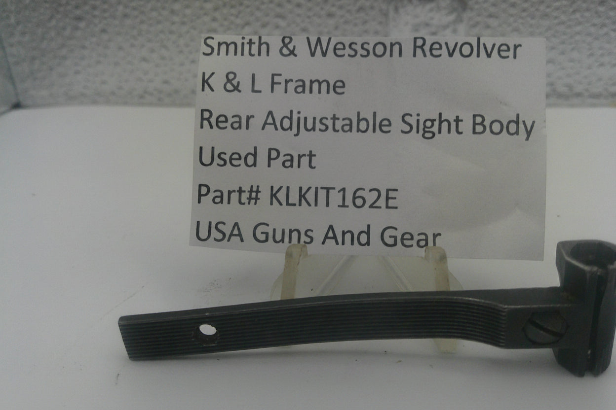 A used black metal part for a Smith & Wesson revolver rear adjustable sight body, displayed on a clear stand with a white label card showing part details.