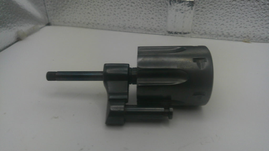 A black plastic and metal mechanical component, likely a lock cylinder or similar hardware part, shown on a white surface against a textured gray background.