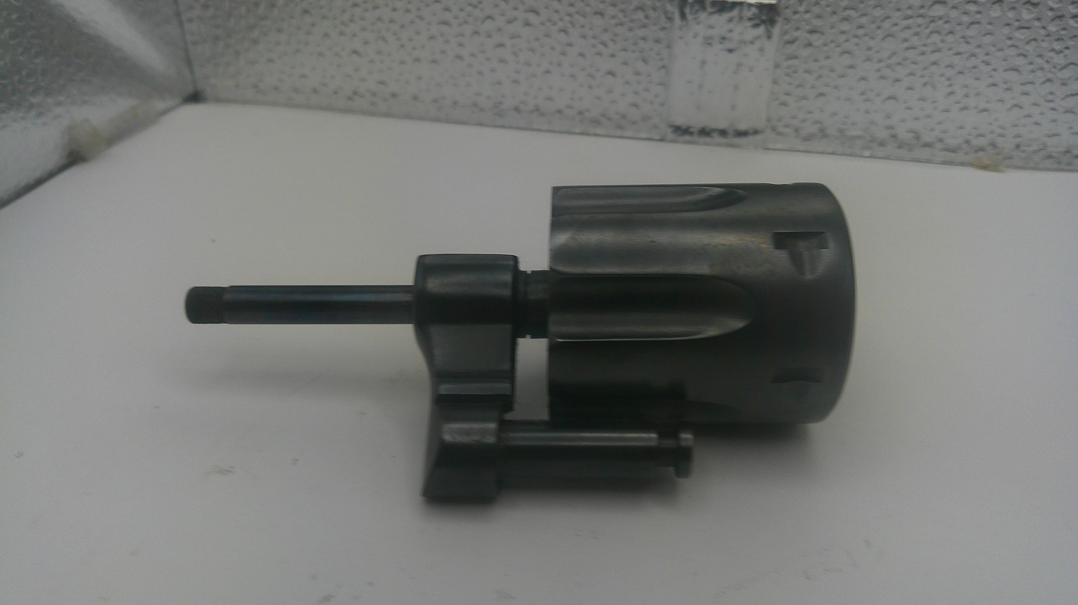 A black plastic and metal mechanical component, likely a lock cylinder or similar hardware part, shown on a white surface against a textured gray background.