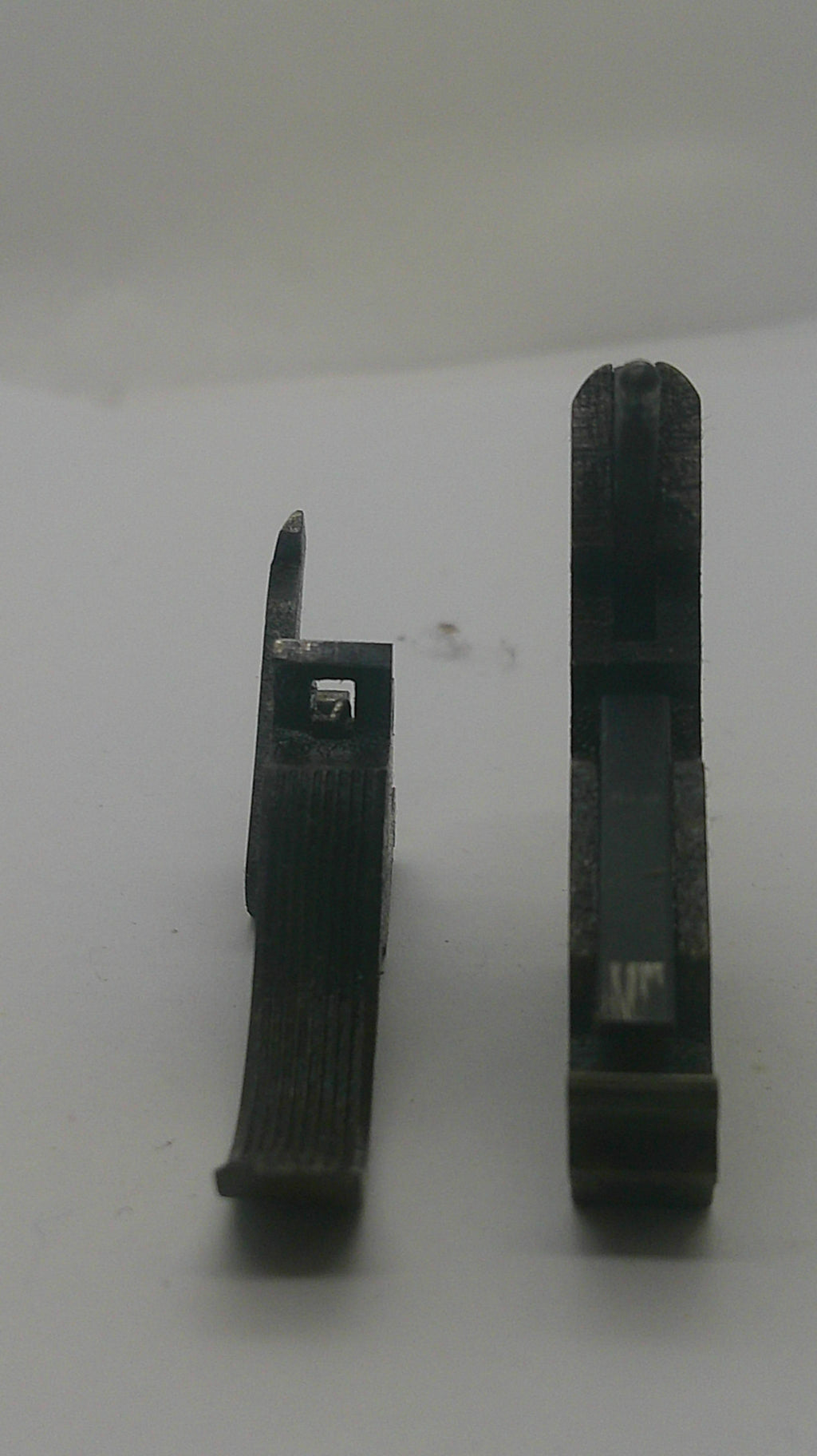 Two small black plastic or metal tool pieces photographed on a plain light background, one above the other.