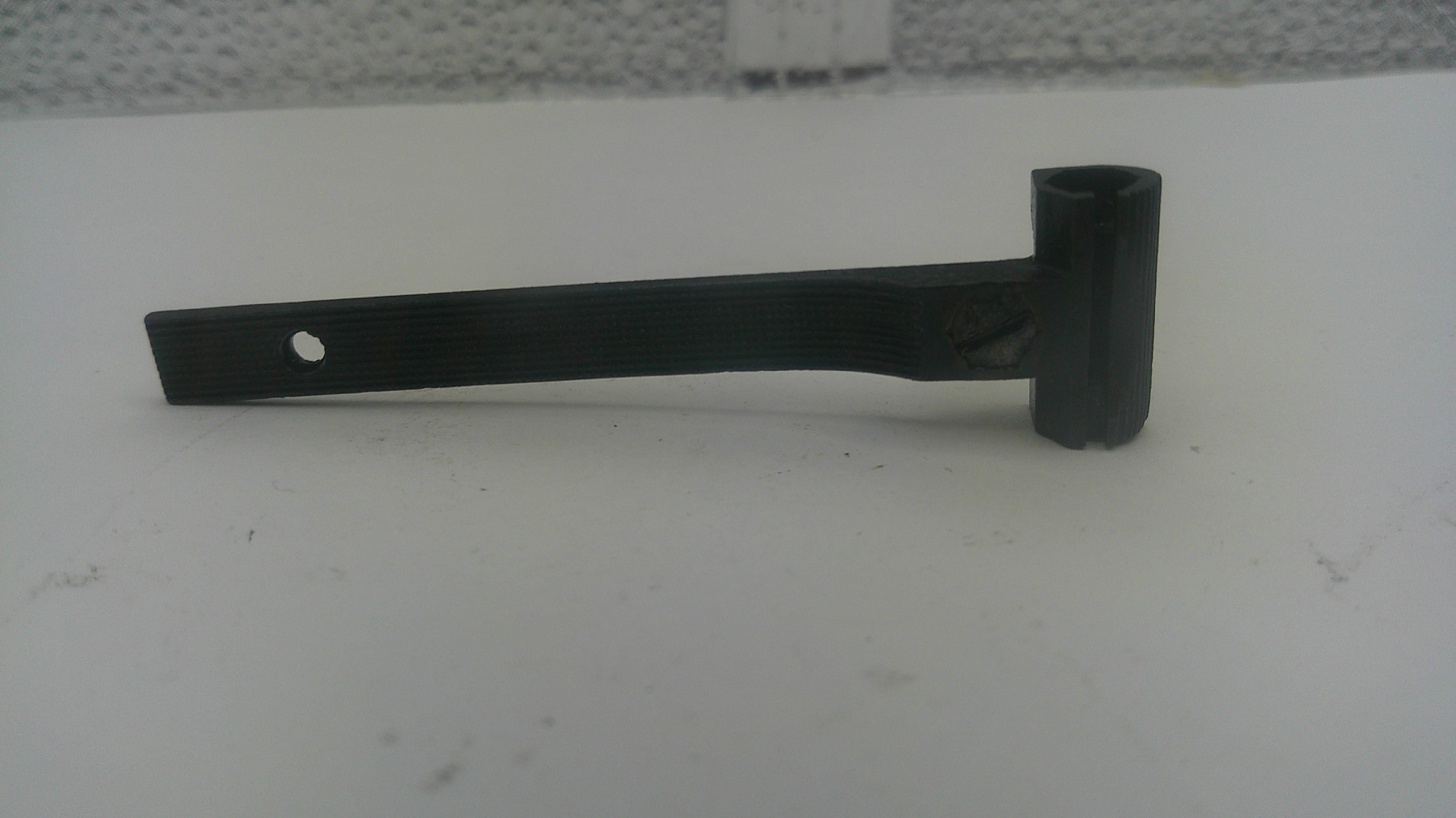 A black metal pipe bend with a cylindrical shank and a single hole on the flat end, resting on a white surface.