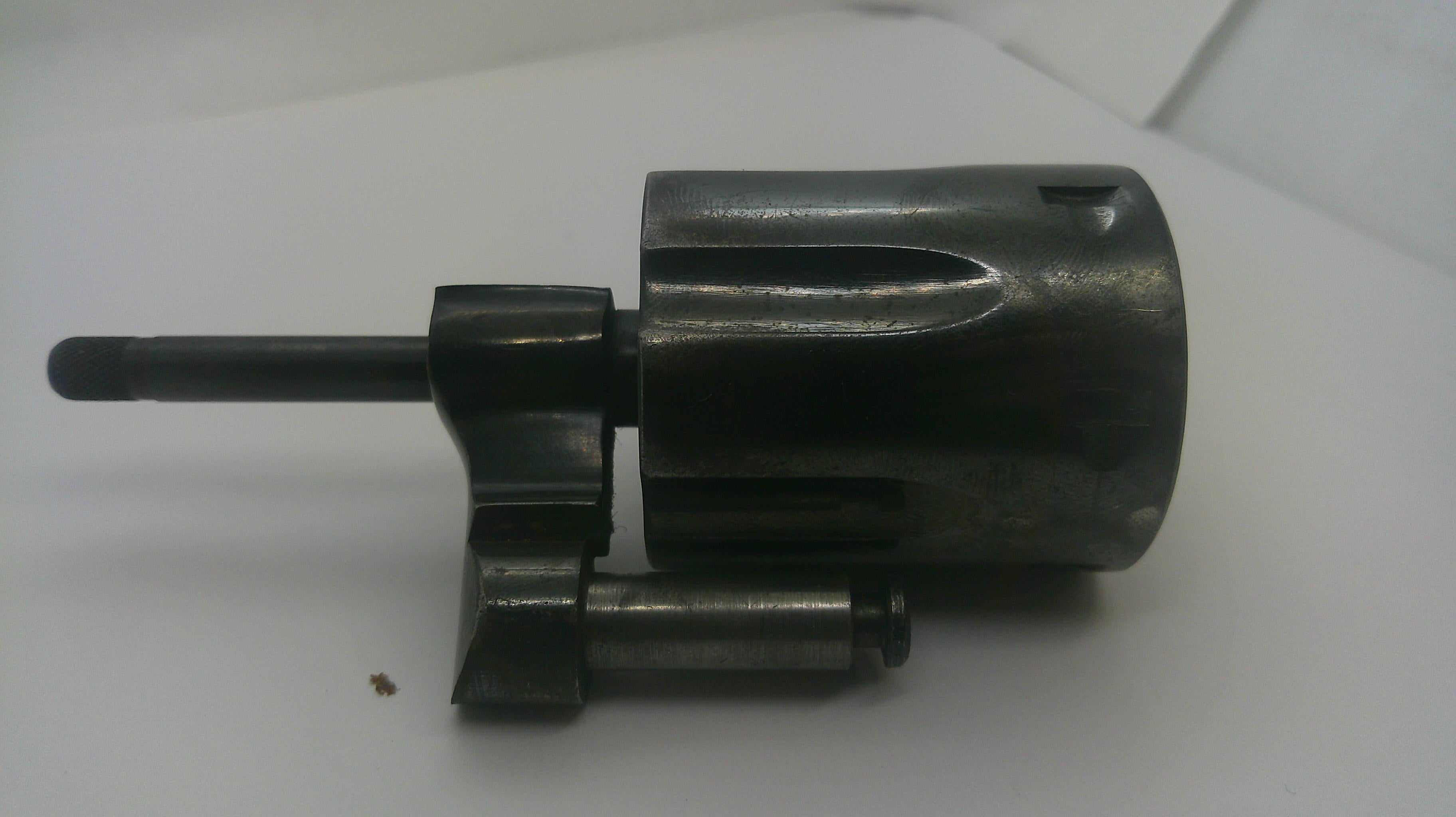 A dark metallic mechanical component, likely a lock cylinder or gun lock part, shown on a plain white background.