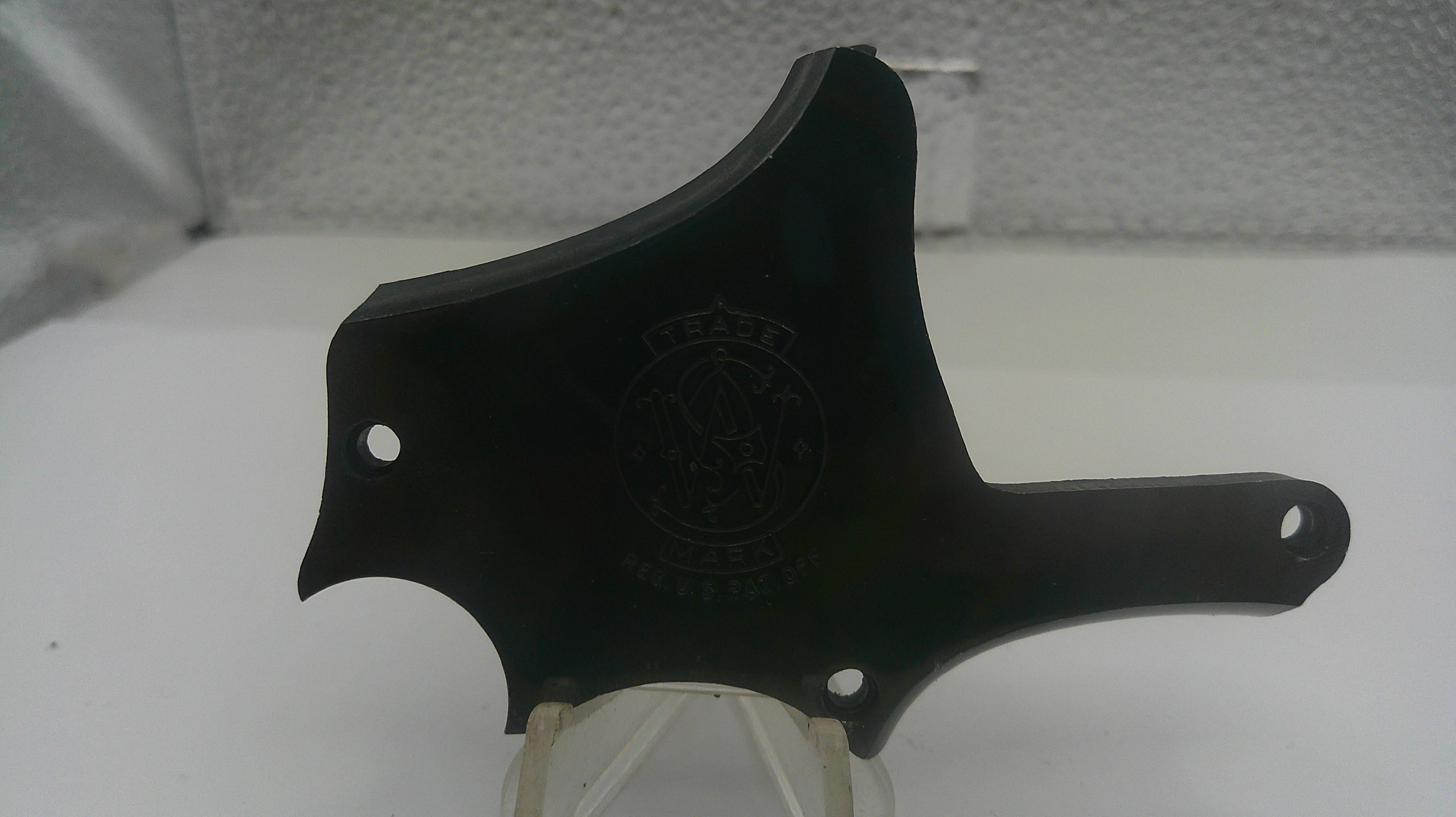 A black plastic knife guard or handle component with a circular logo embossed in the center, displayed on a clear stand against a white textured background.