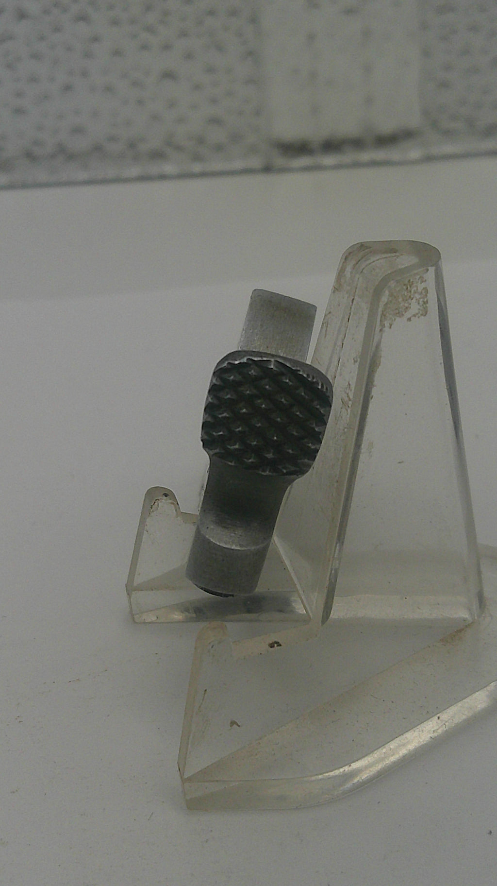 Clear plastic component with textured black knob on a white background