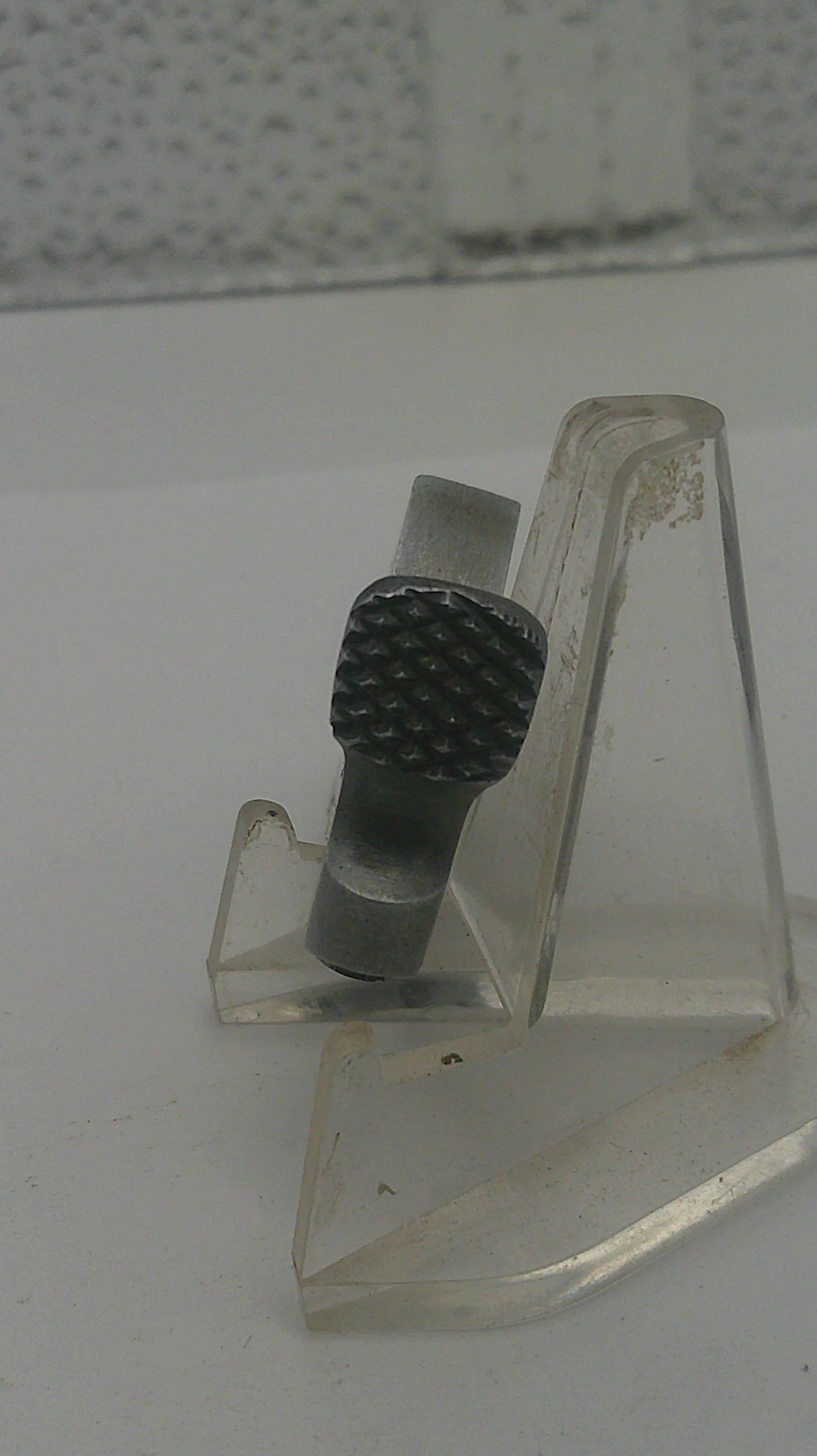Clear plastic component with textured black knob on a white background