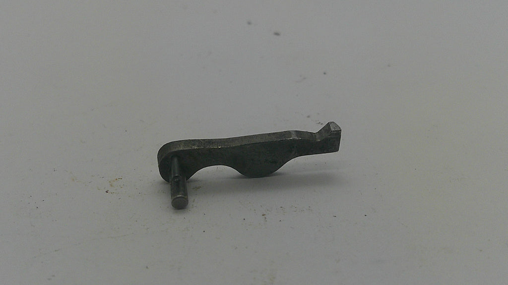 A small dark metal mechanical part or pin with a curved body and flat tip, photographed on a plain light gray surface.