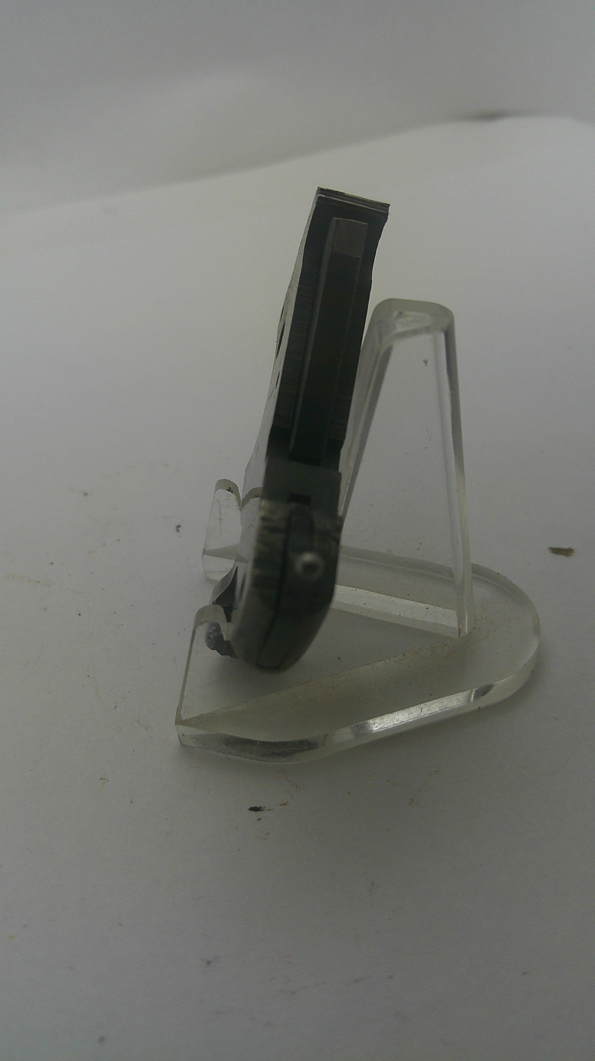 A clear plastic wall hook with a black plastic hanging tab, mounted on a plain white wall.
