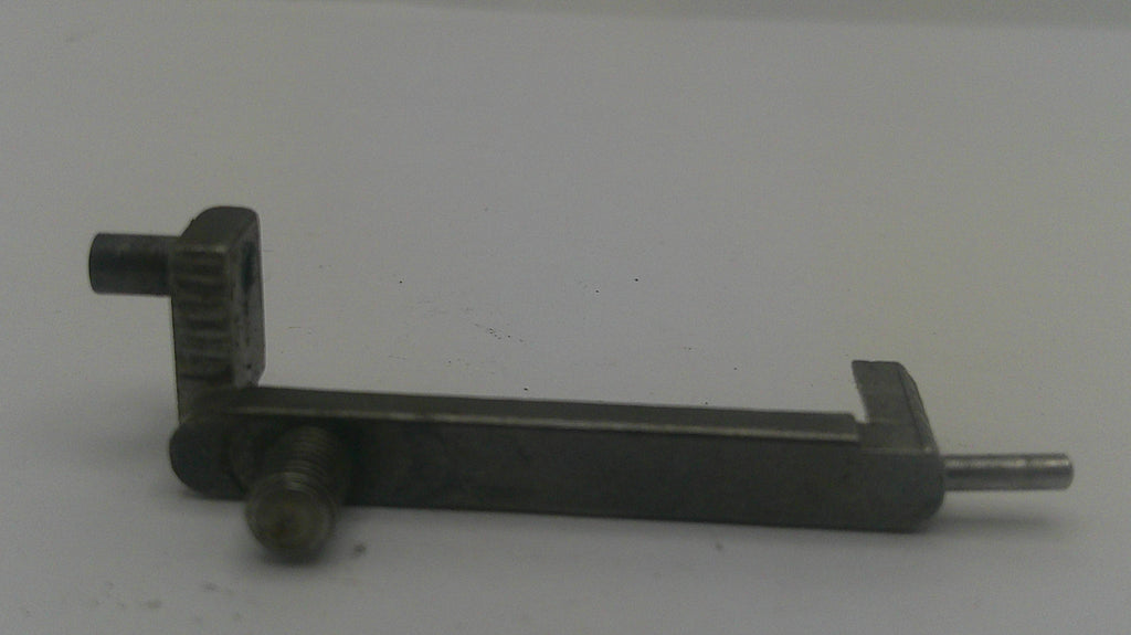 A dark metal mechanical component or tool part with a long horizontal bar, a perpendicular arm, and a protruding pin, photographed against a plain light background.