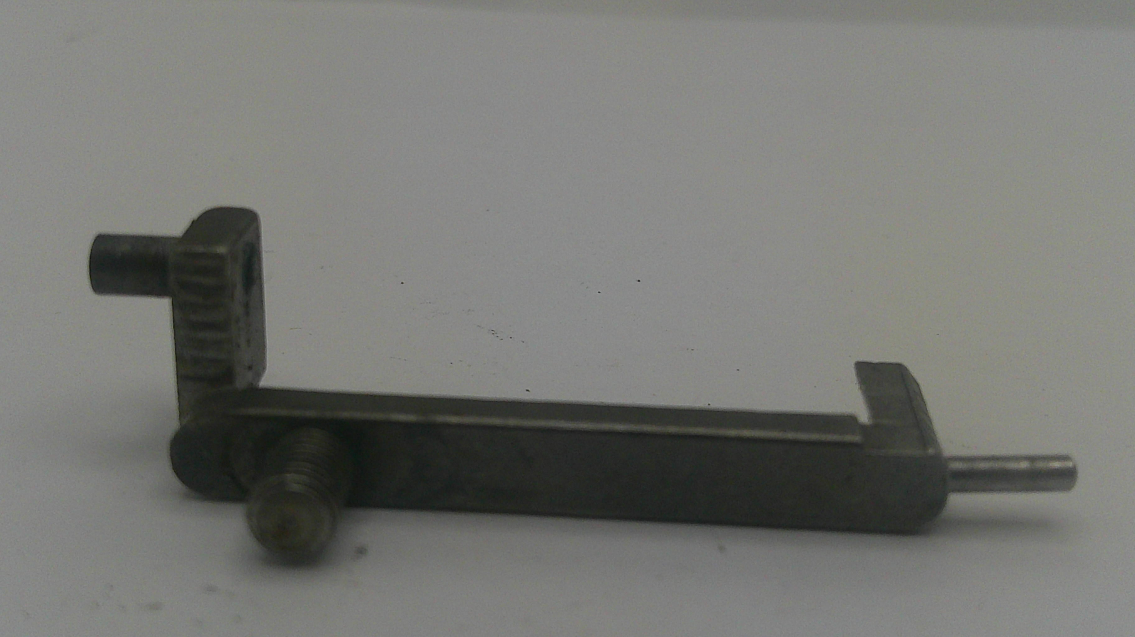 A dark metal mechanical component or tool part with a long horizontal bar, a perpendicular arm, and a protruding pin, photographed against a plain light background.